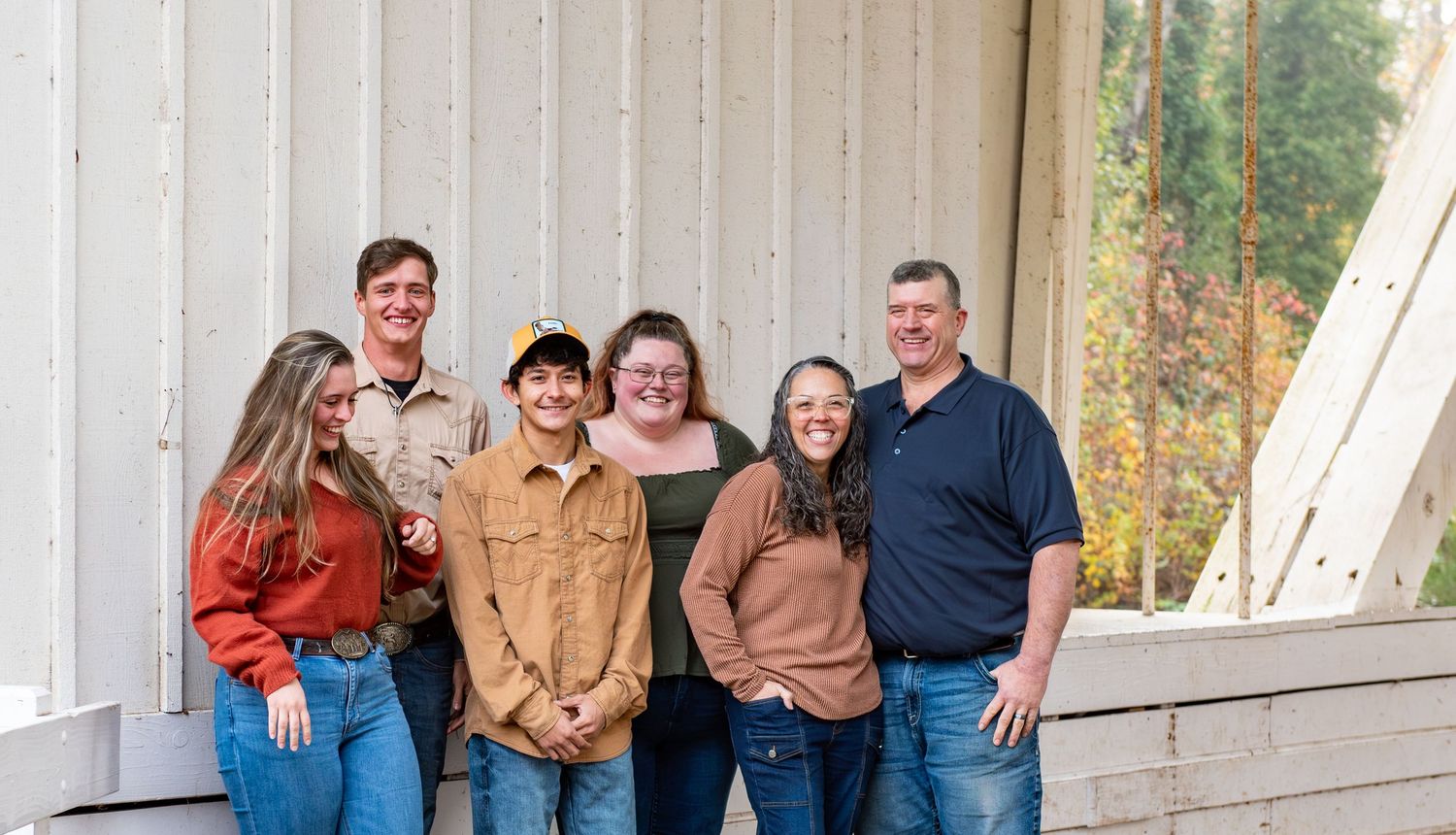 A group of people in casual fall attire pose together on a rustic wooden covered bridge during an autumn photo session. Location Stayton, OR