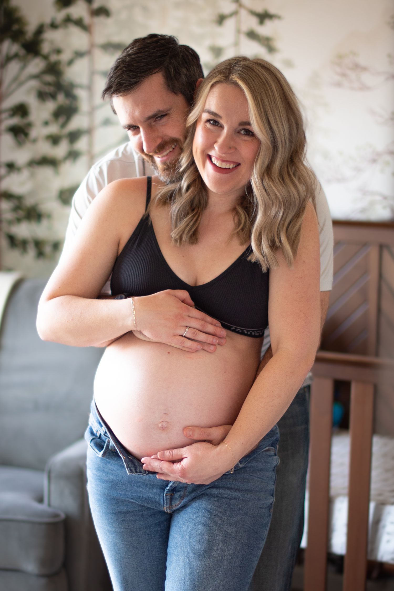 A couple shares an intimate moment as they embrace and smile while standing together in a casual home setting.