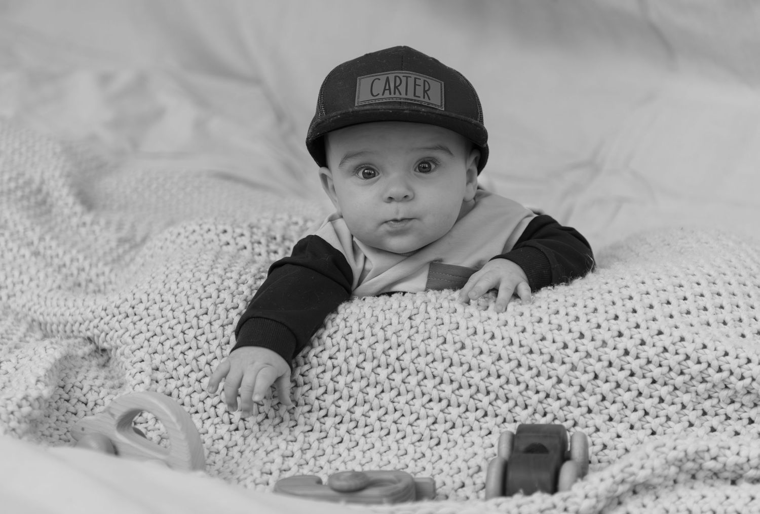 Six month milestone image with baby laying on a blanket, smiling and interacting with parents. Neutral backdrop with lettering. Salem, OR.