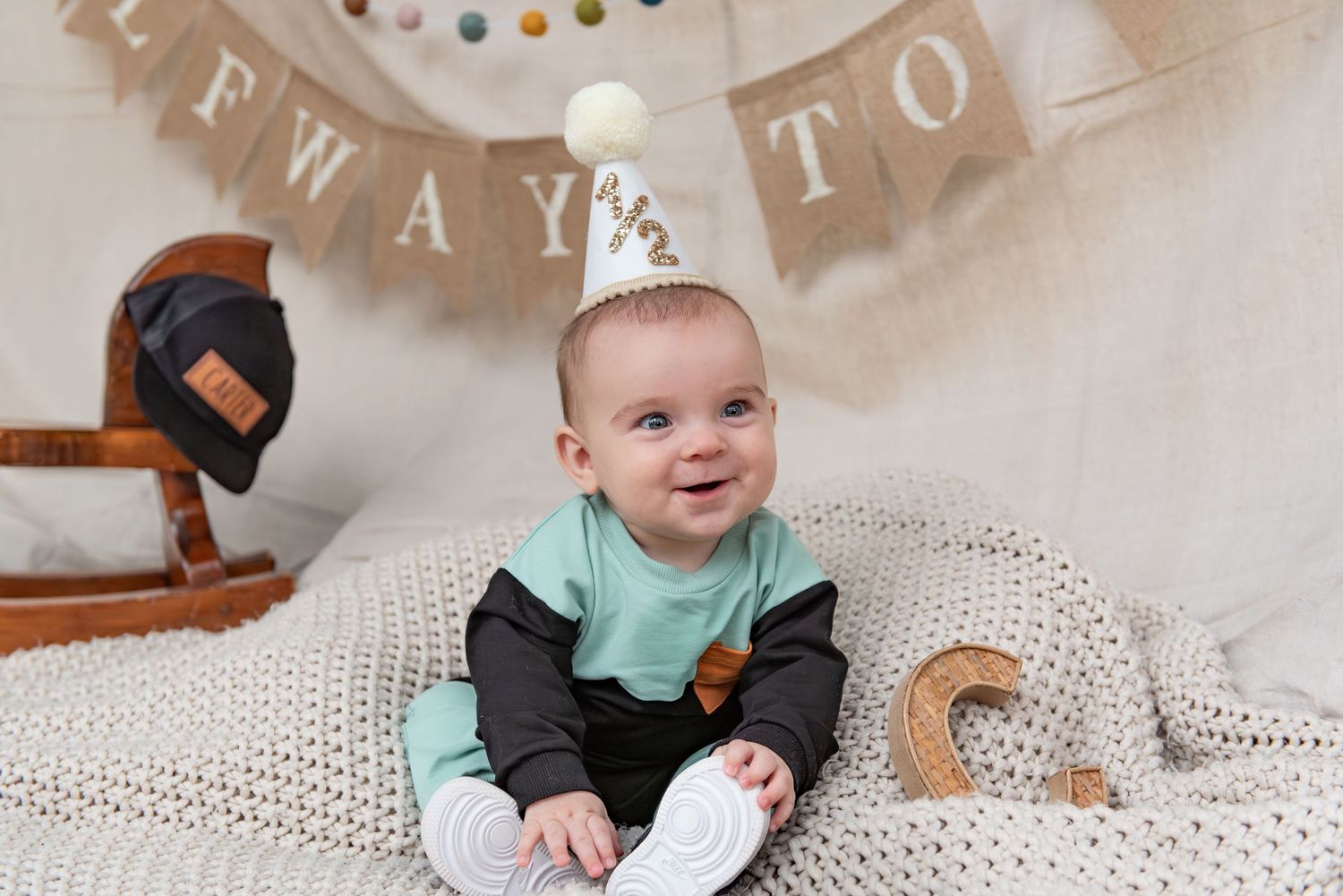 Six month milestone image with baby laying on a blanket, smiling and interacting with parents. Neutral backdrop with lettering. Salem, OR.