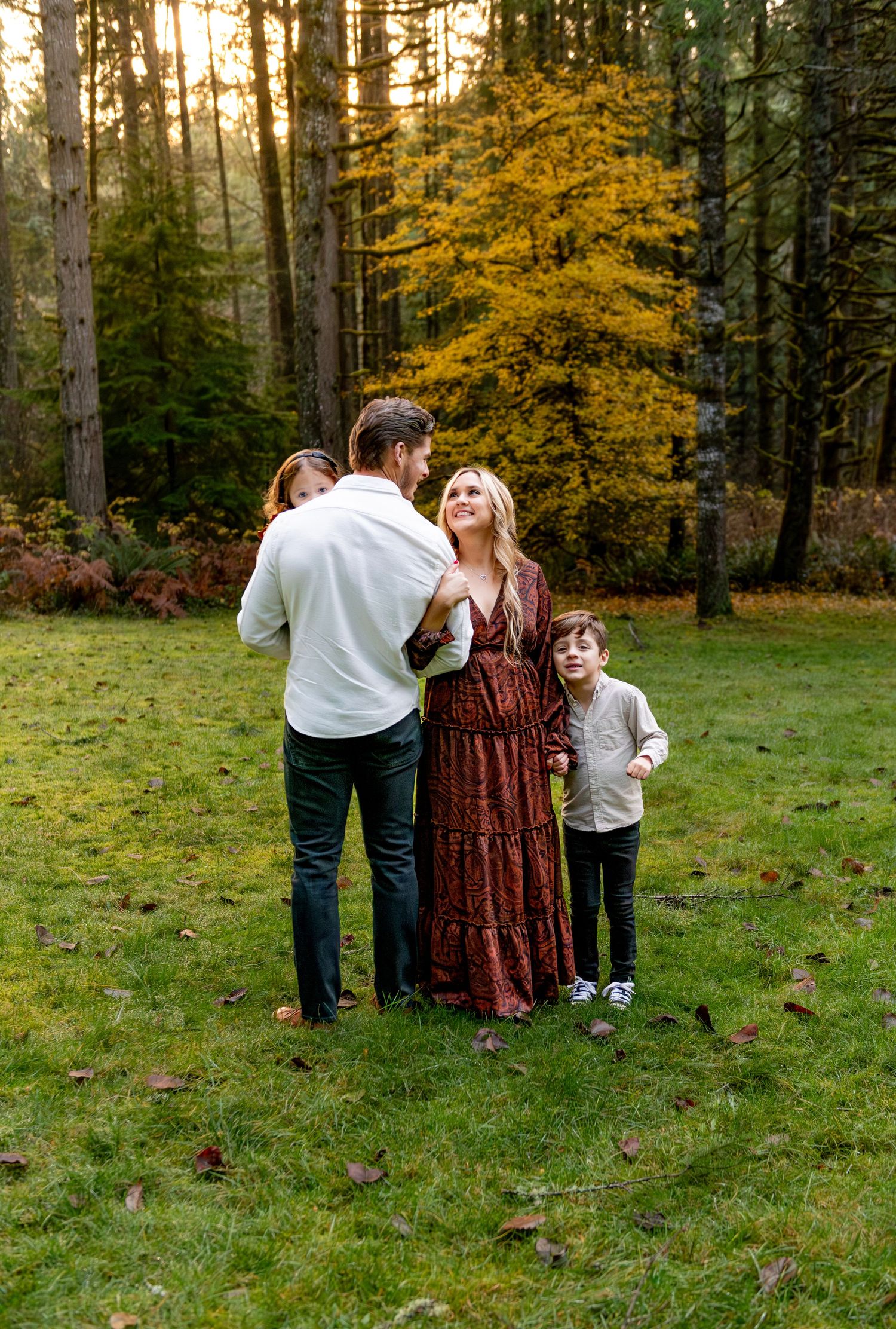 A family shares tender moments together in a sunlit autumn forest with golden leaves and evergreen trees. Silver Falls State Park, OR