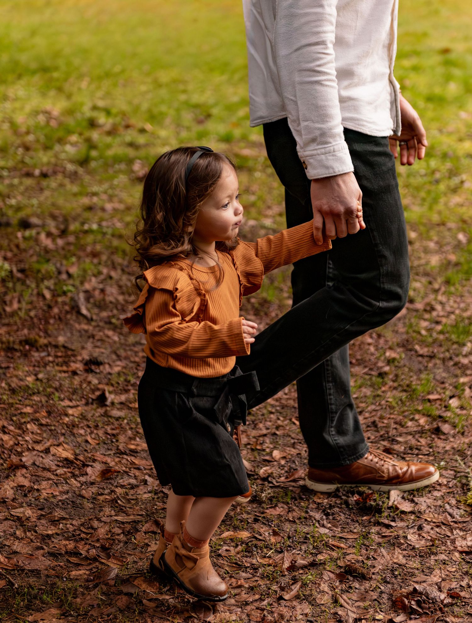 Two people walk together through a grassy autumn field with fallen leaves scattered on the ground. Silverton, OR