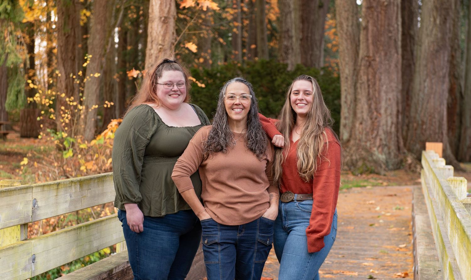 A group of people stand together on a wooden bridge surrounded by tall trees in autumn. located in Stayton, OR