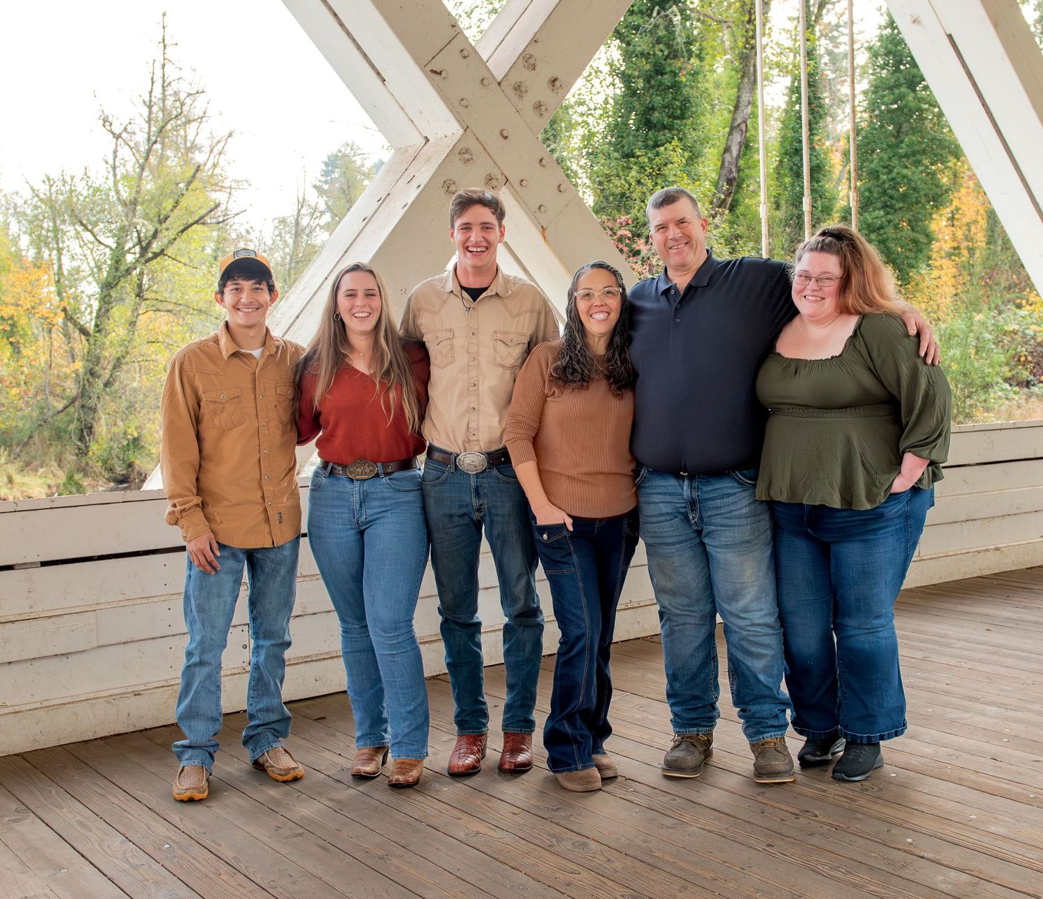 A group of people stand together on a wooden covered bridge surrounded by tall trees in autumn. located in Stayton, OR