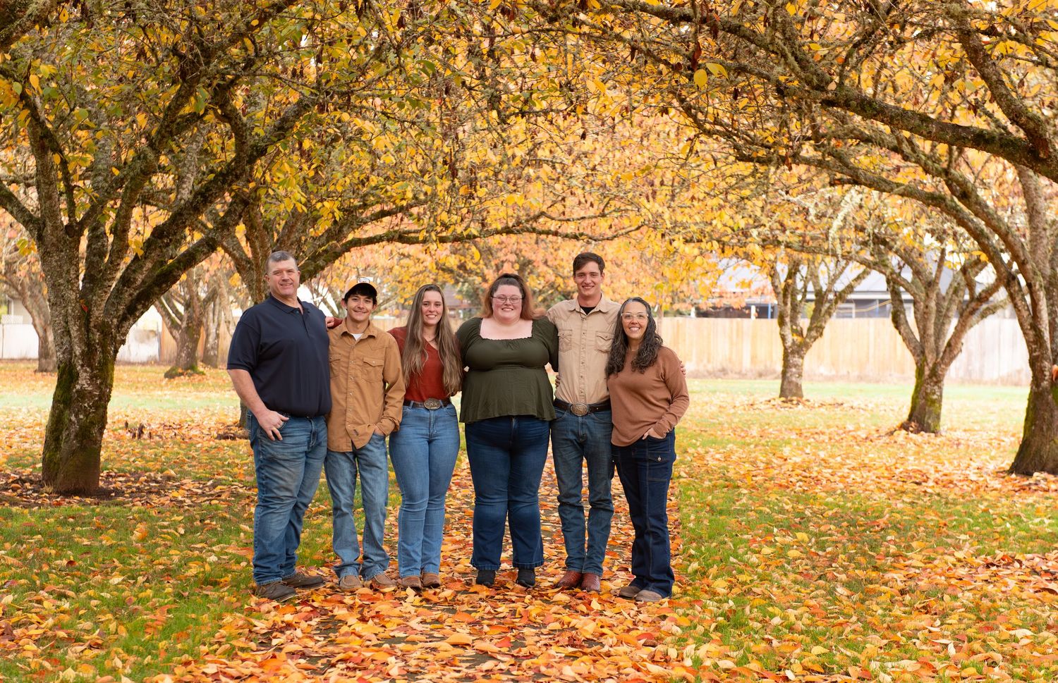 Group poses together under autumn trees with golden leaves and fallen foliage on the ground during a fall photo session. Stayton, OR