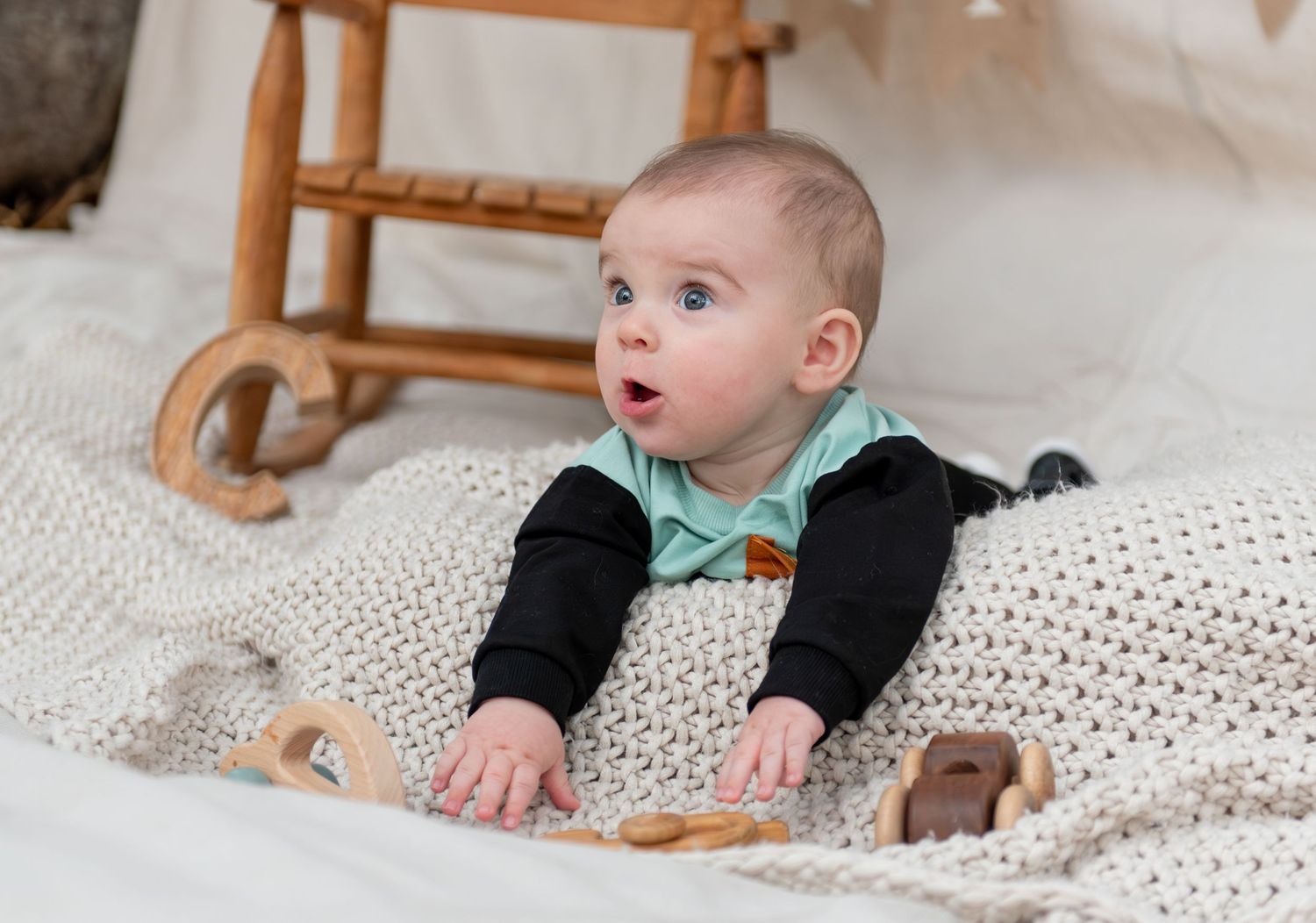 Six month milestone image with baby laying on a blanket, smiling and interacting with parents. Neutral backdrop with lettering. Salem, OR.