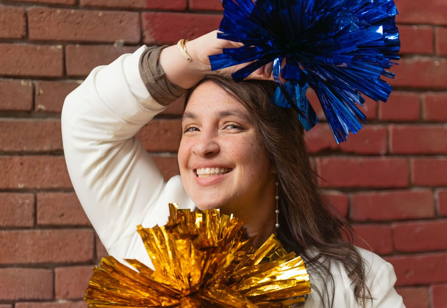 Headshot of woman with pompoms blue and gold with red brick background, for branding images, located in Salem, OR.