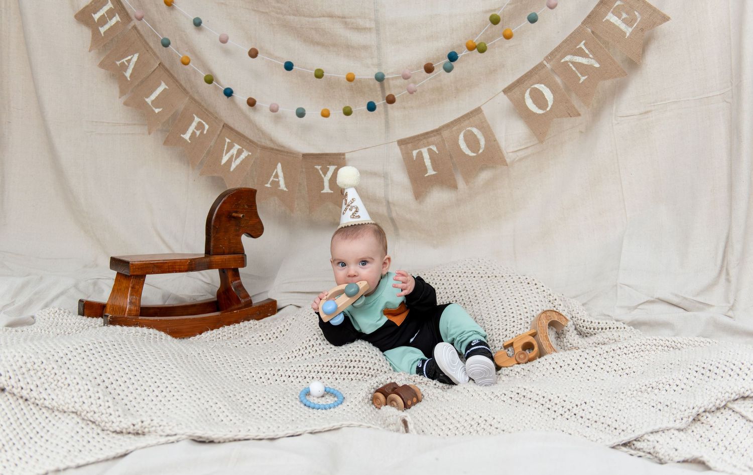 Six month milestone image with baby laying on a blanket, smiling and interacting with parents. Neutral backdrop with lettering. Salem, OR.