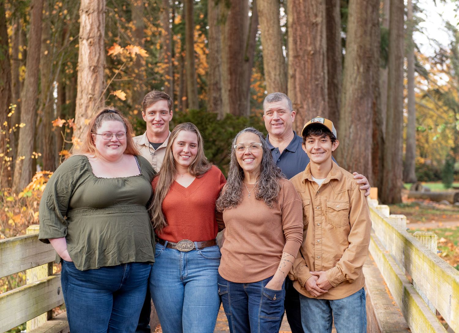 A group of people stand together on a wooden bridge surrounded by tall trees in autumn. located in Stayton, OR