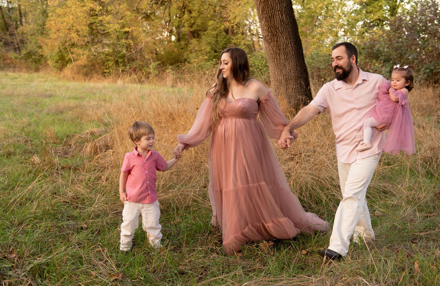 Family of four portrait located in a field with fall colored trees in the background and natural golden hour light. Located in Salem, OR