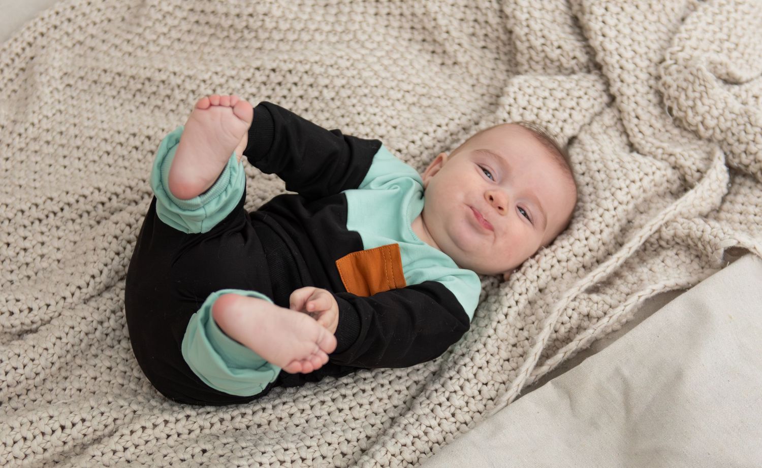 Six month milestone image with baby laying on a blanket, smiling and interacting with parents. Neutral backdrop with lettering. Salem, OR.