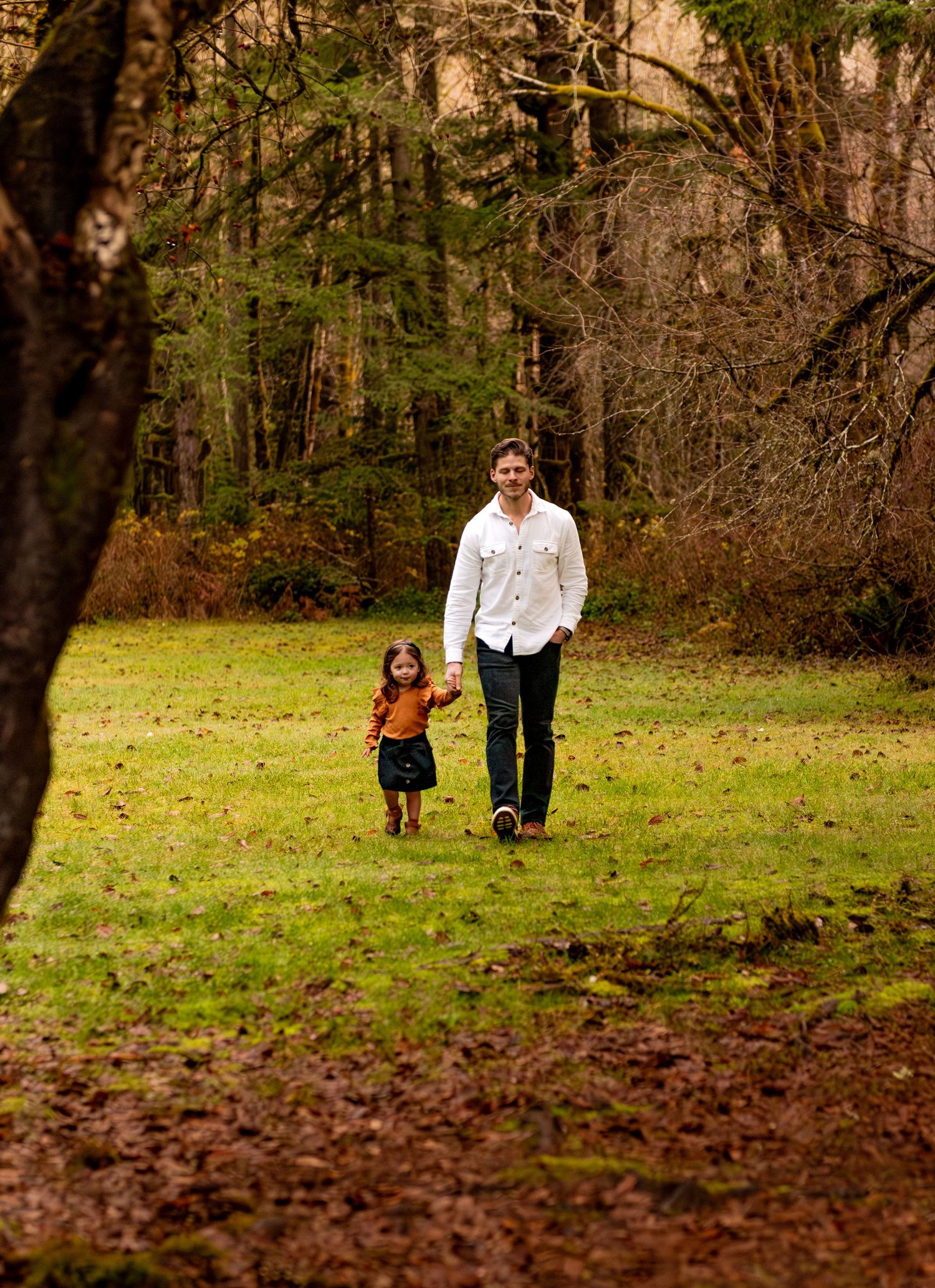 Two people walk together through a grassy autumn field with fallen leaves scattered on the ground. Silverton, OR