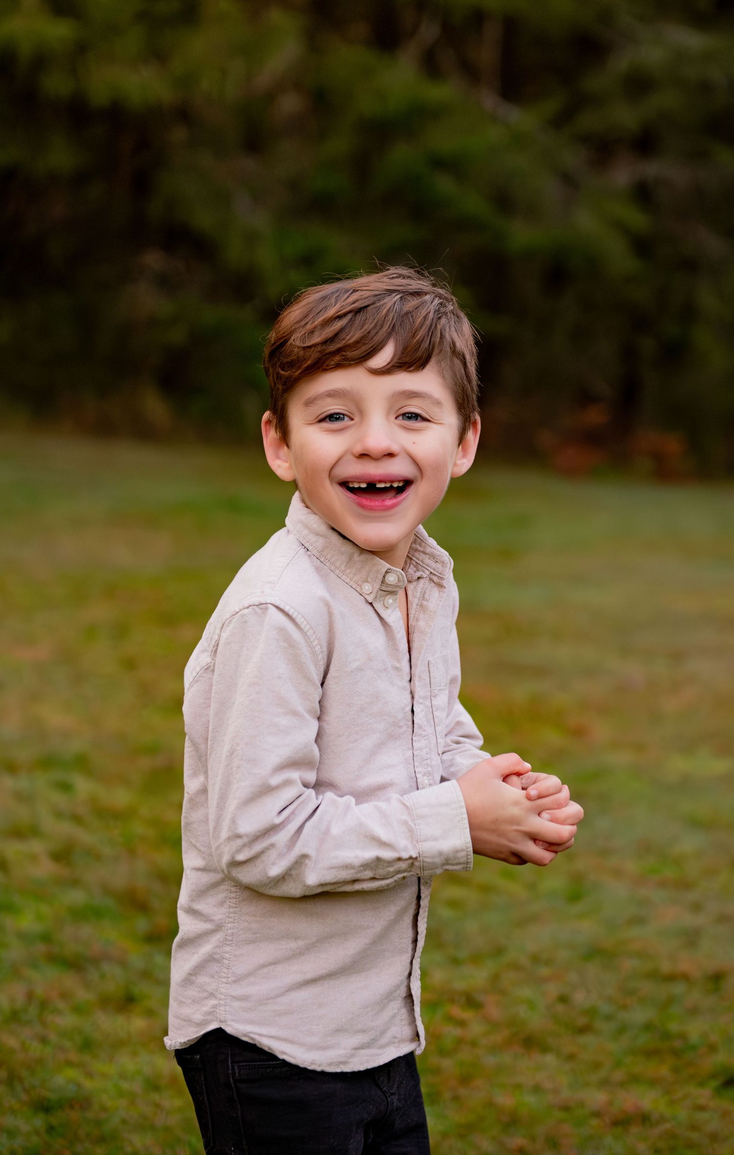 A young child in a beige button-down shirt laughs joyfully while playing outdoors in a grassy area. Silver Falls State Park OR