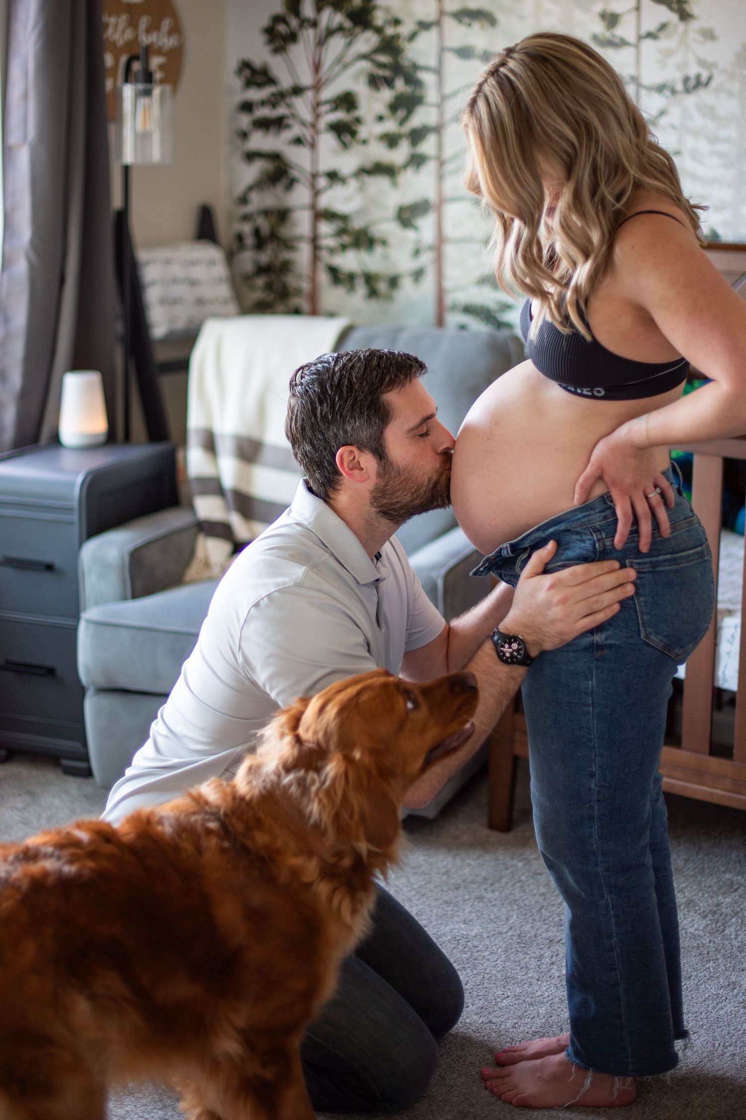 A couple and their golden retriever share a tender moment with a pregnant belly in a nursery room setting. Located in Salem, OR