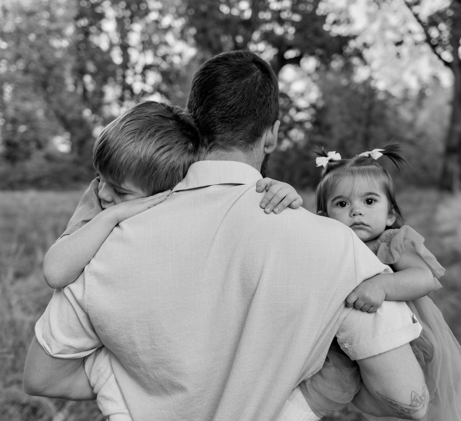 Dad with two children posing in a field with trees in the background in Salem, Or