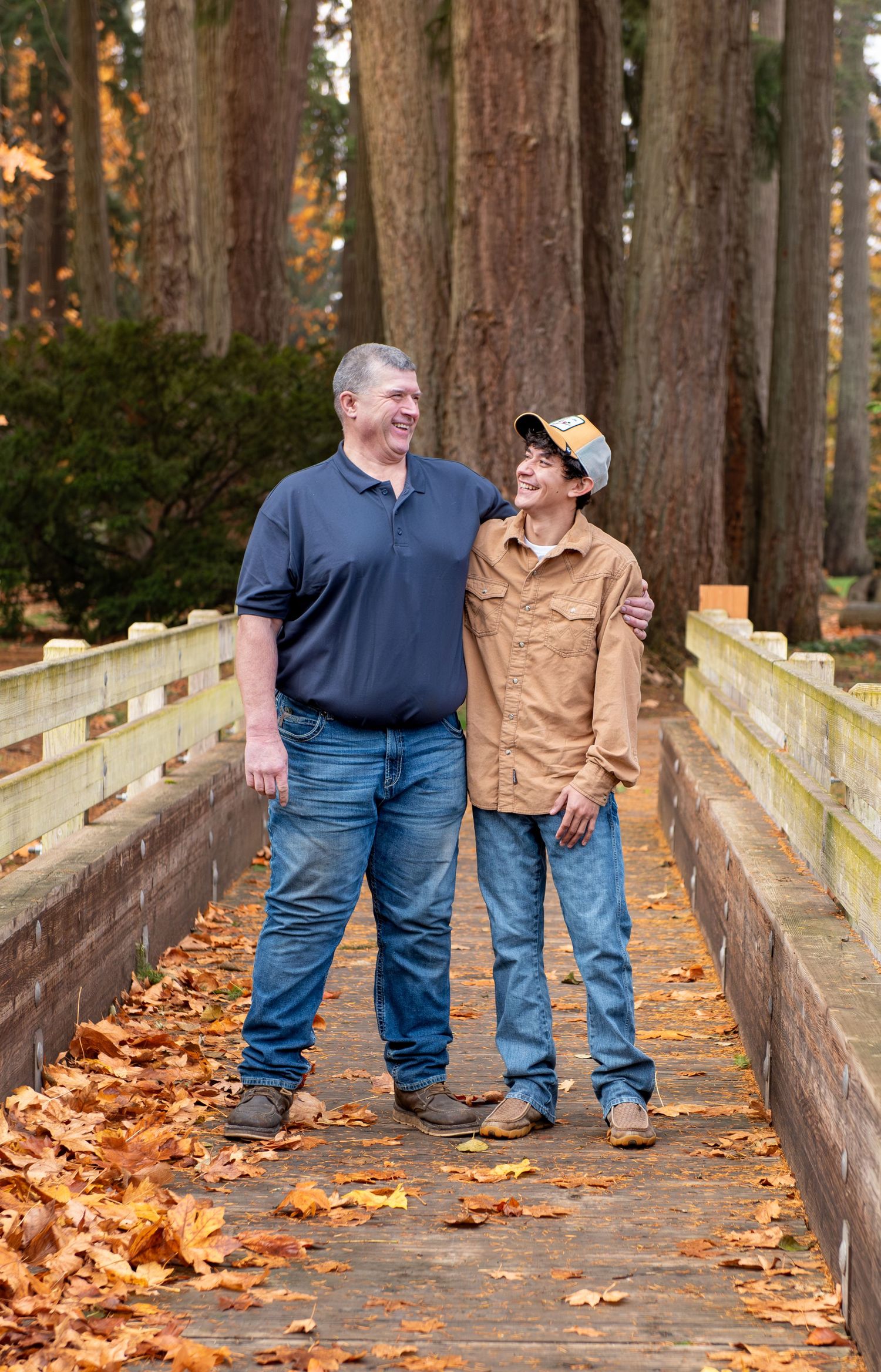Two people share a happy moment while walking on a wooden bridge covered in autumn leaves through a forest. located in Stayton, OR