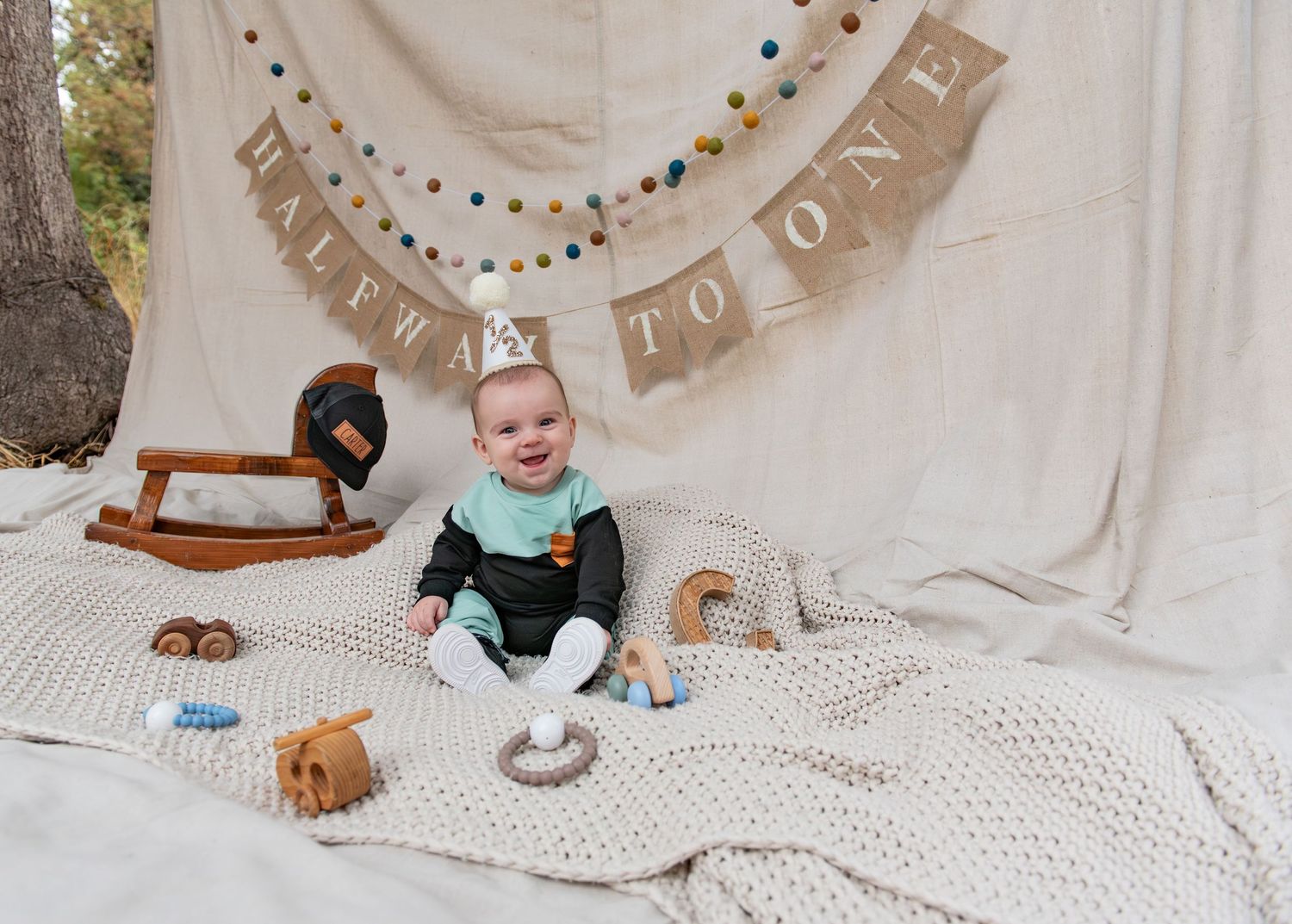 Six month milestone image with baby laying on a blanket, smiling and interacting with parents. Neutral backdrop with lettering. Salem, OR.