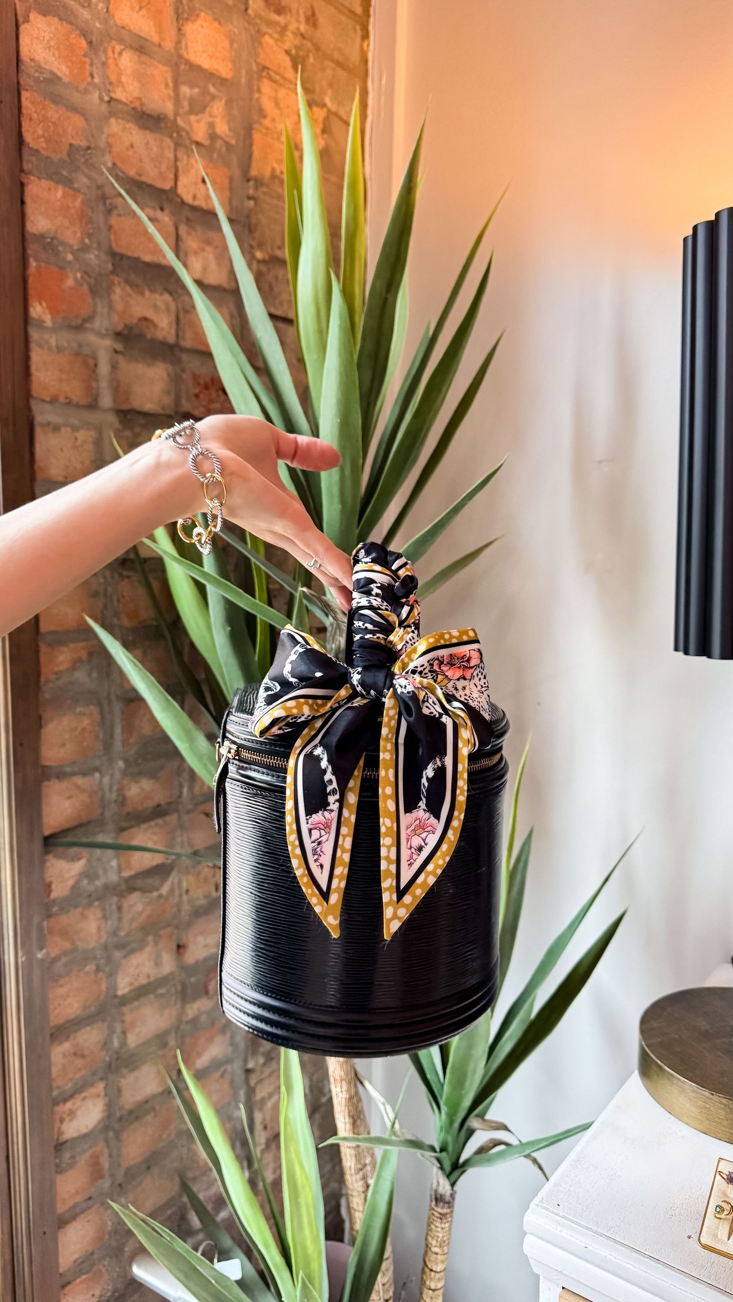 A woman's hand holding a vintage Chanel purse styled with a twilly accessory scarf braided on the handle for an elevated look for the brand.