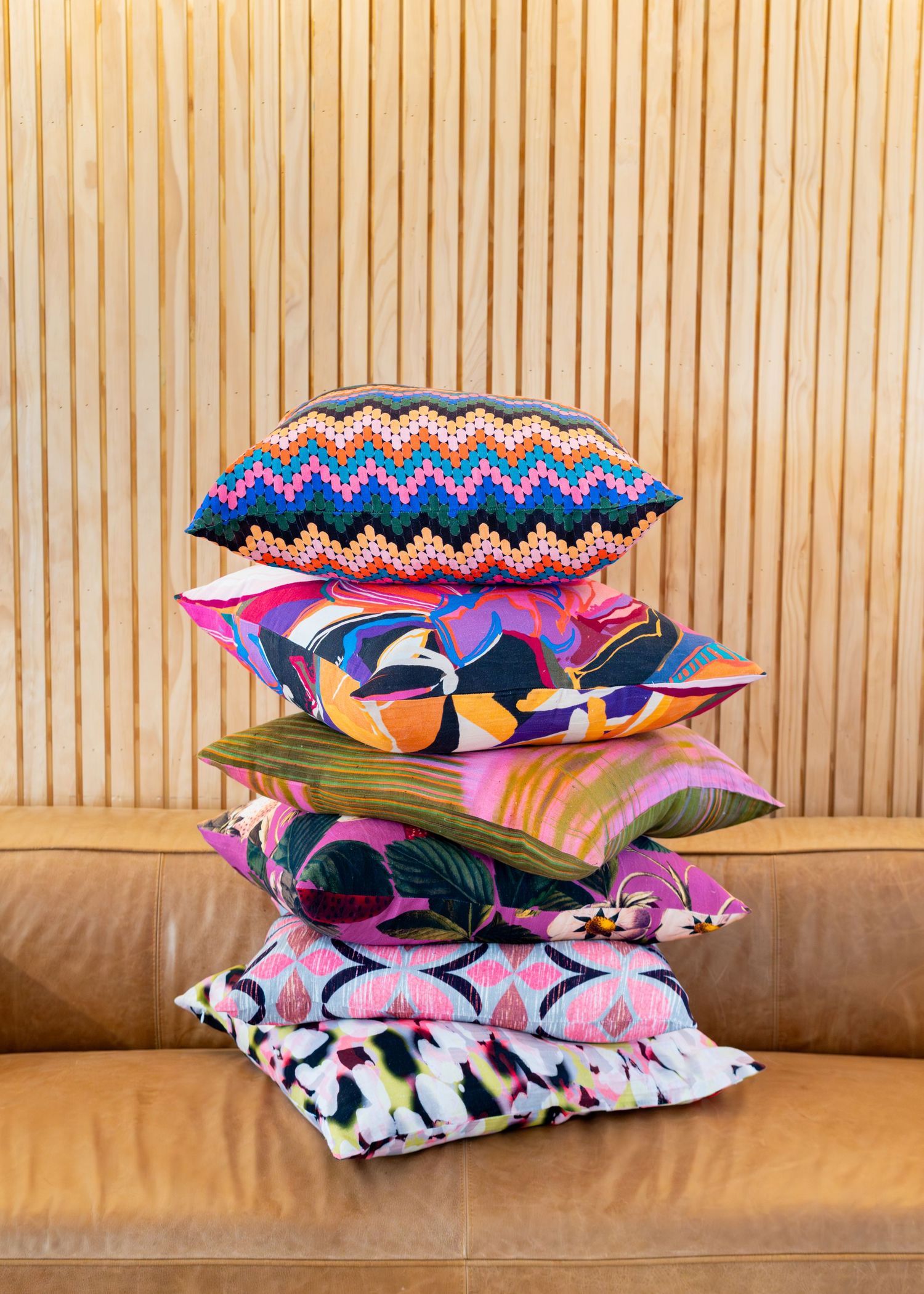 Different-sized pillows displayed on a leather couch showcase different fabric prints for a brand in a fun way.