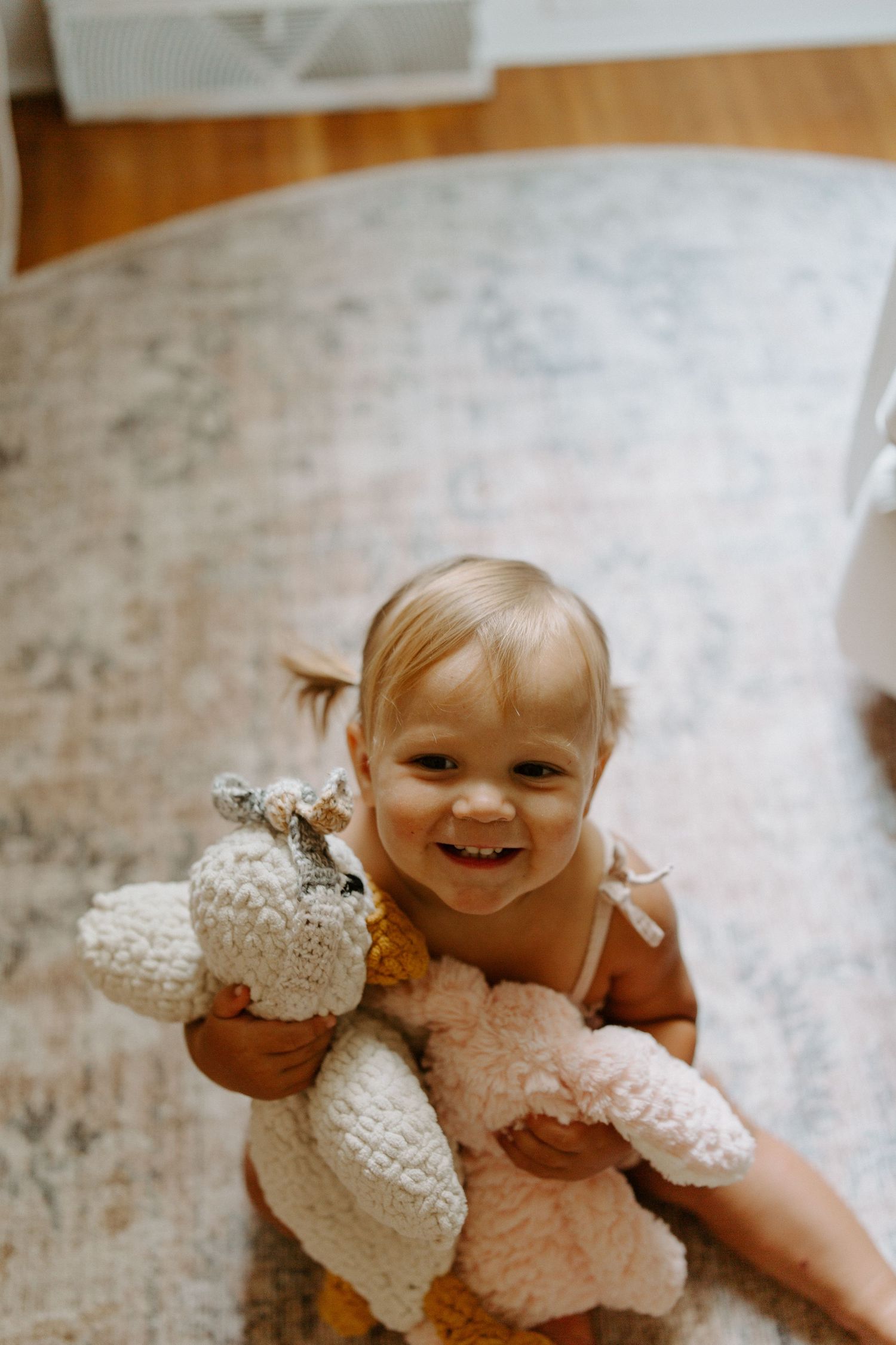 A smiling toddler plays with a plush teddy bear on a patterned rug.