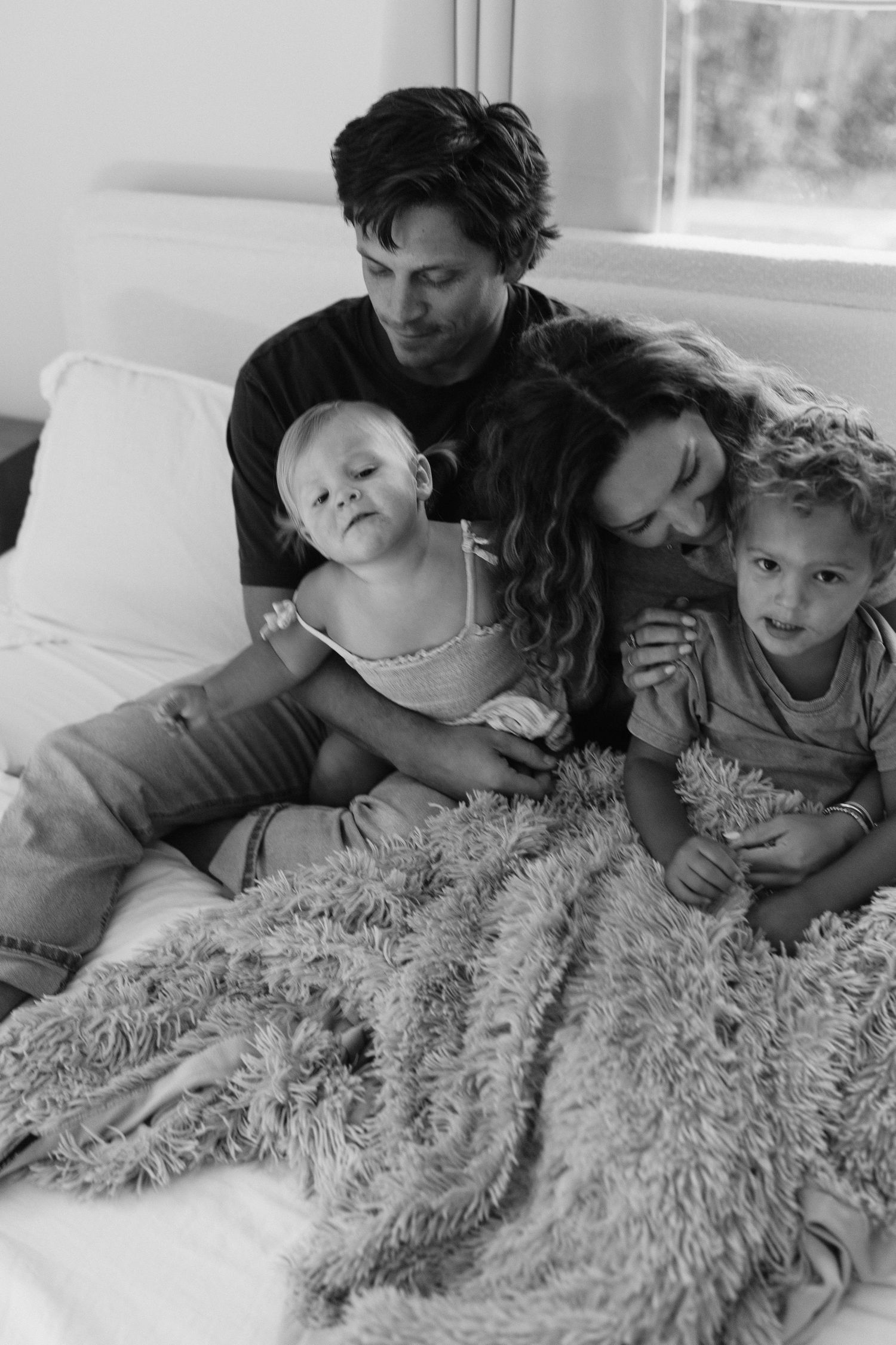 A black and white candid family photo showing tender moments on a fluffy bed.