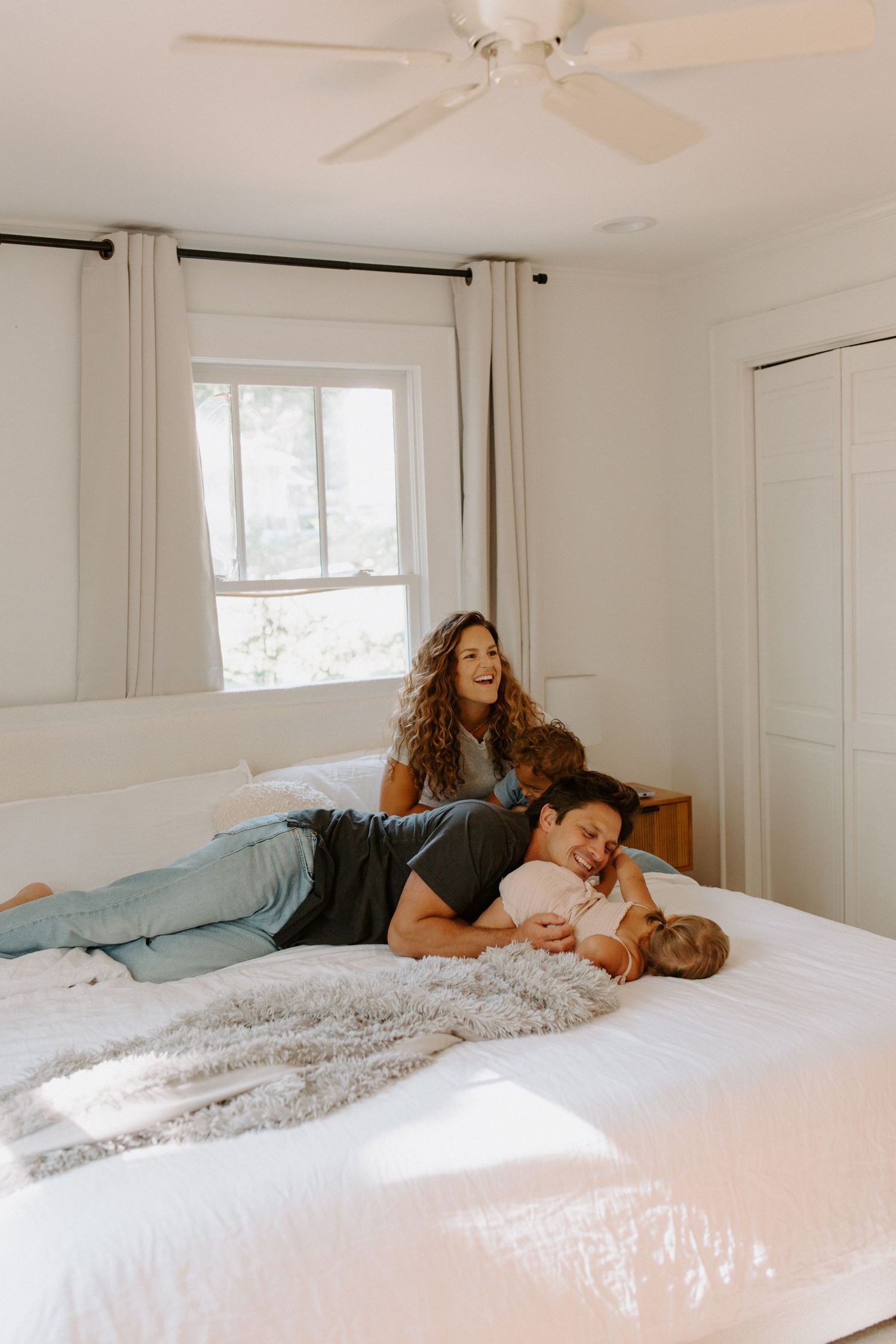A cozy family moment on a white bed with natural light streaming through the window.