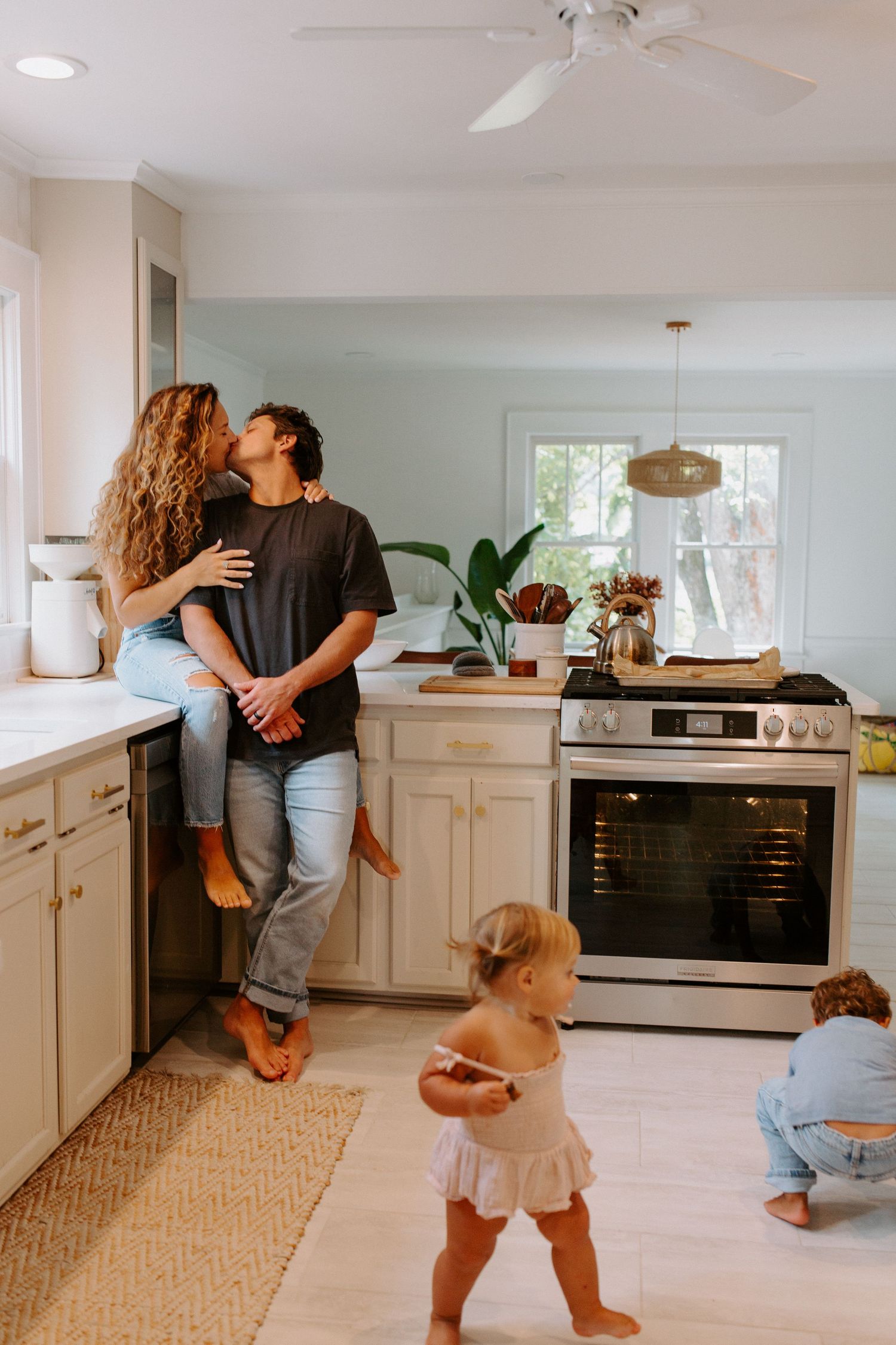 A family shares joyful moments in their modern white kitchen while a toddler plays nearby.