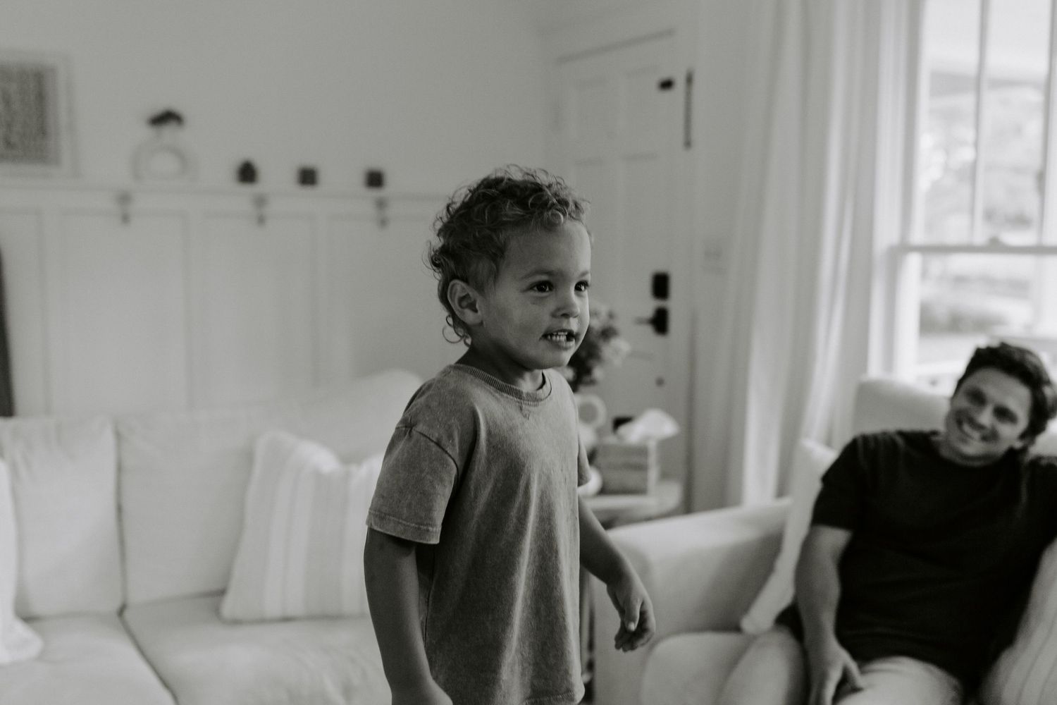 Candid lifestyle moment of playtime and relaxation on a cozy white couch in a bright sunlit room.