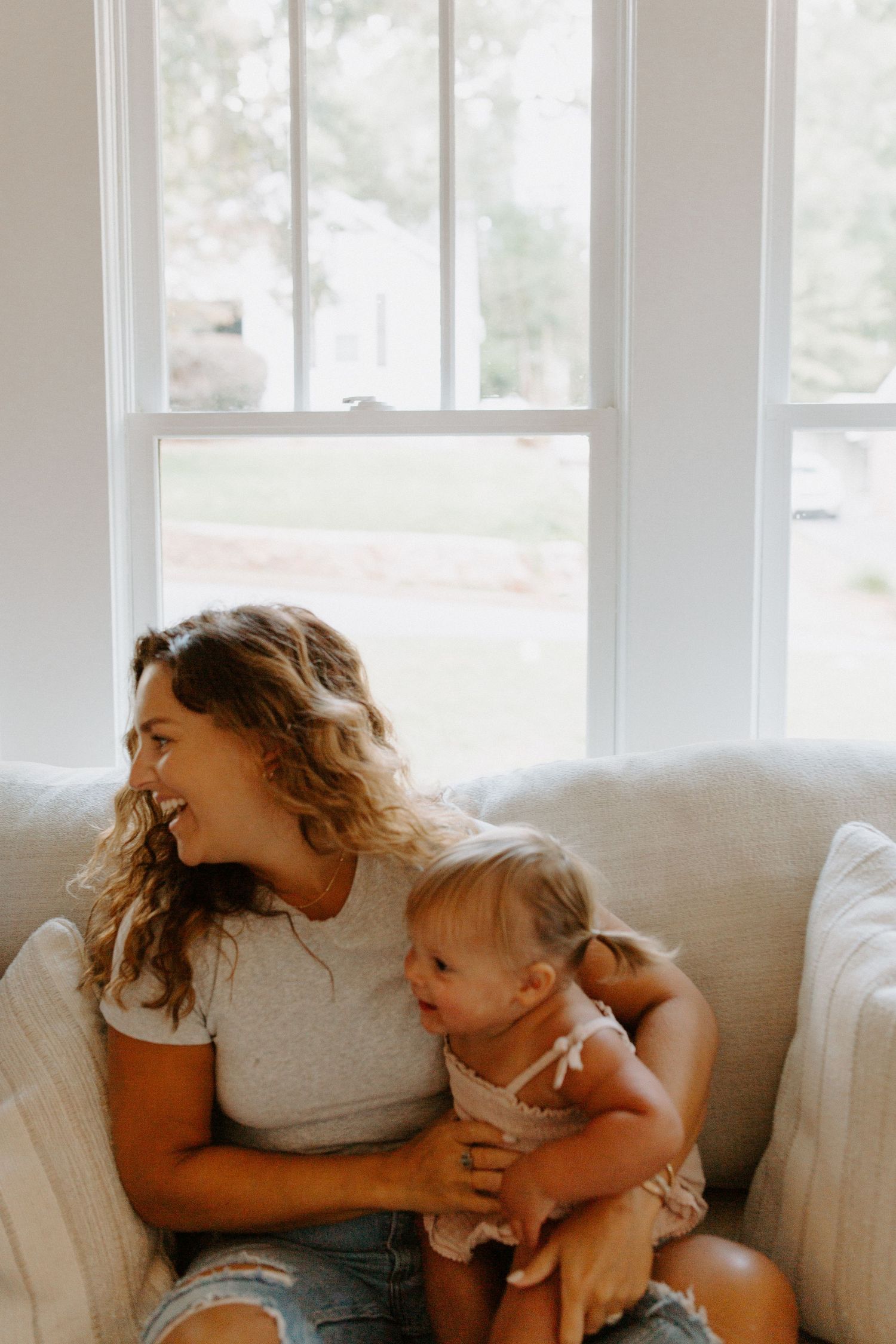 Joyful playtime moment shared on a cozy white sofa with natural light streaming through windows.