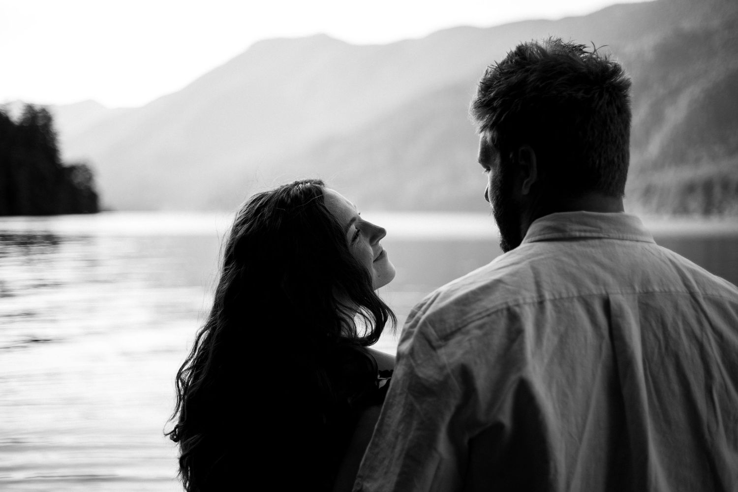 Silhouettes of two people against a mountain landscape and lake at sunset.