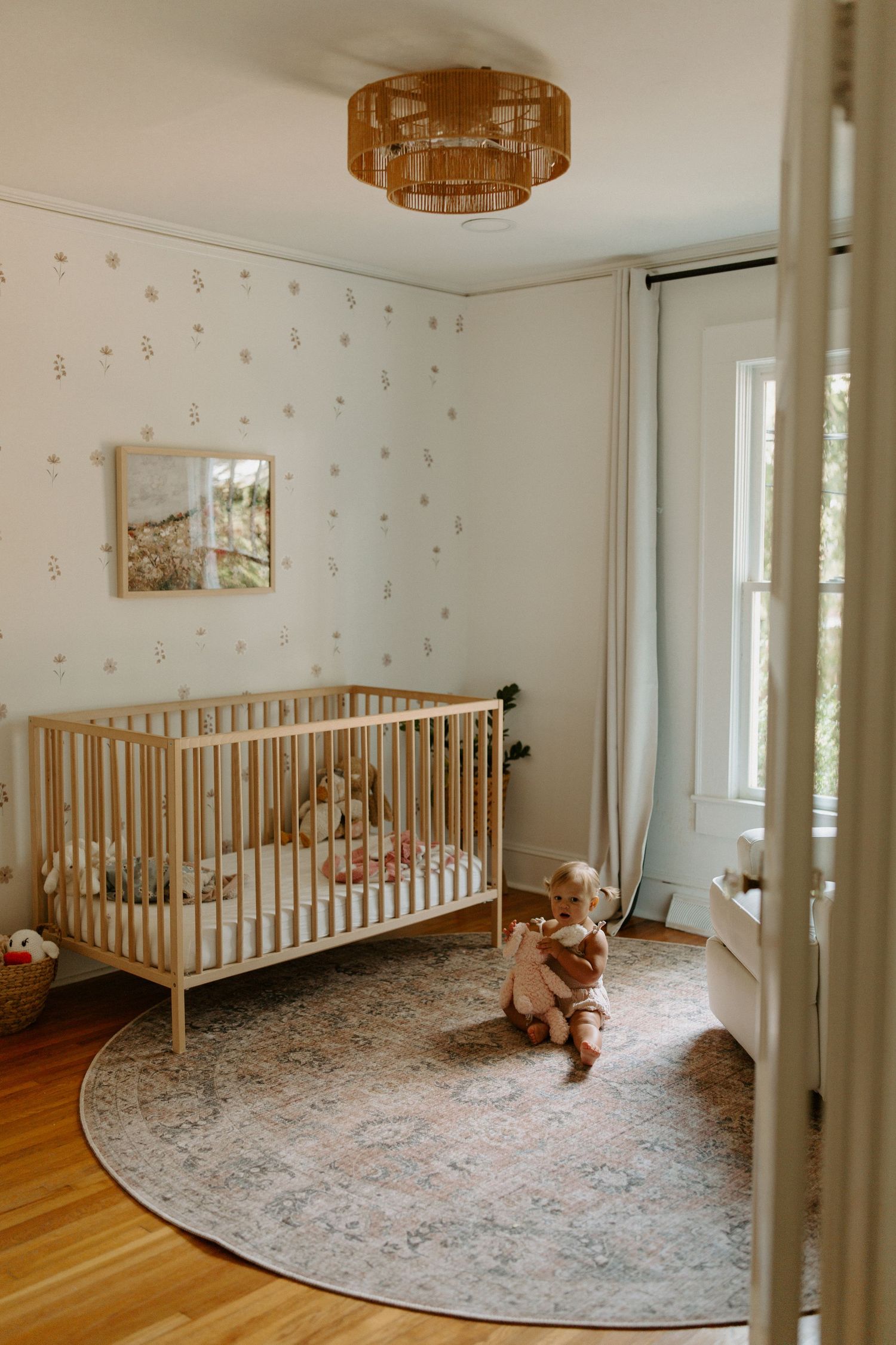 A nursery room with wooden crib, round rug, and decorative lighting fixture.