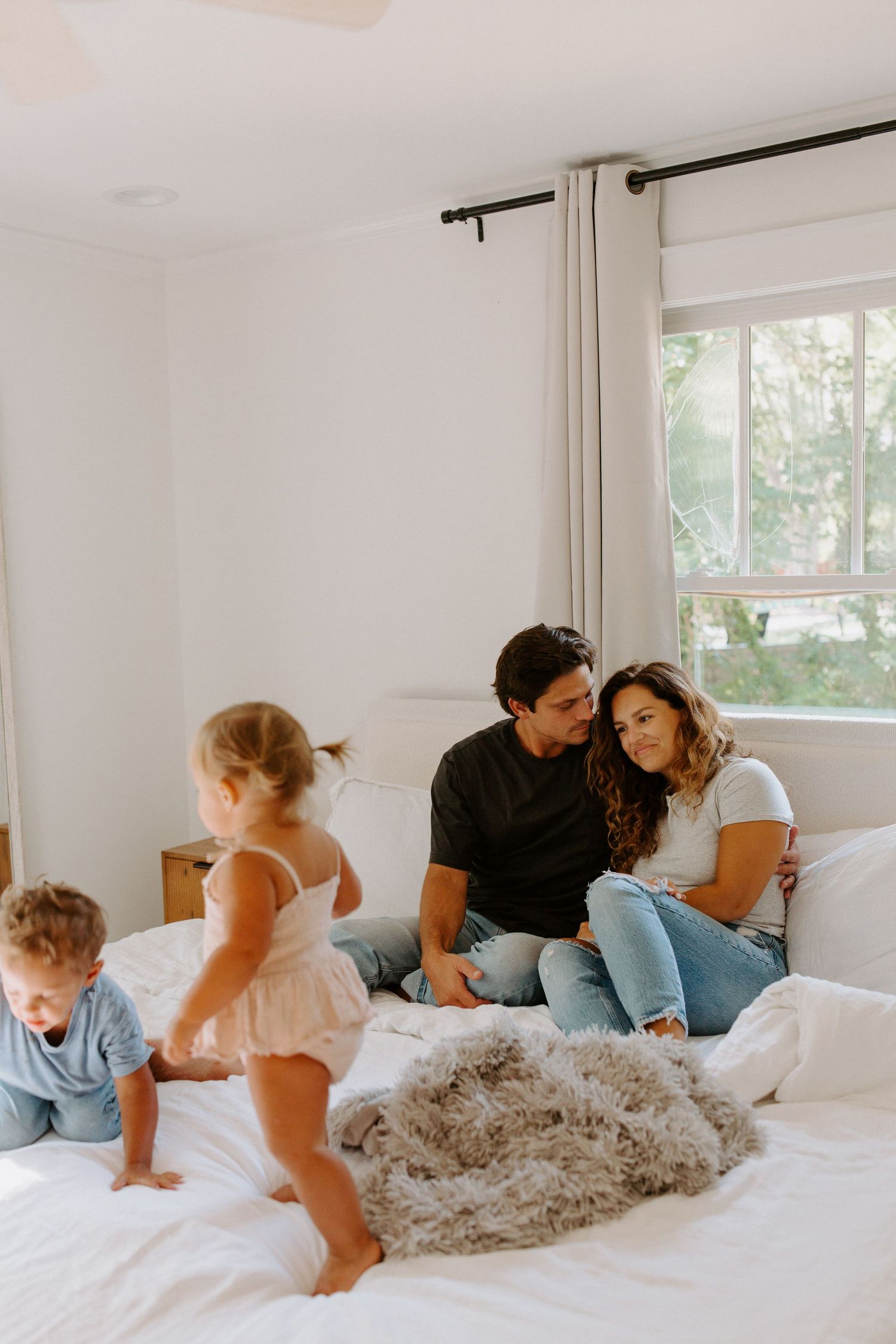 A candid family lifestyle photo showing playful moments on a bright white bed.