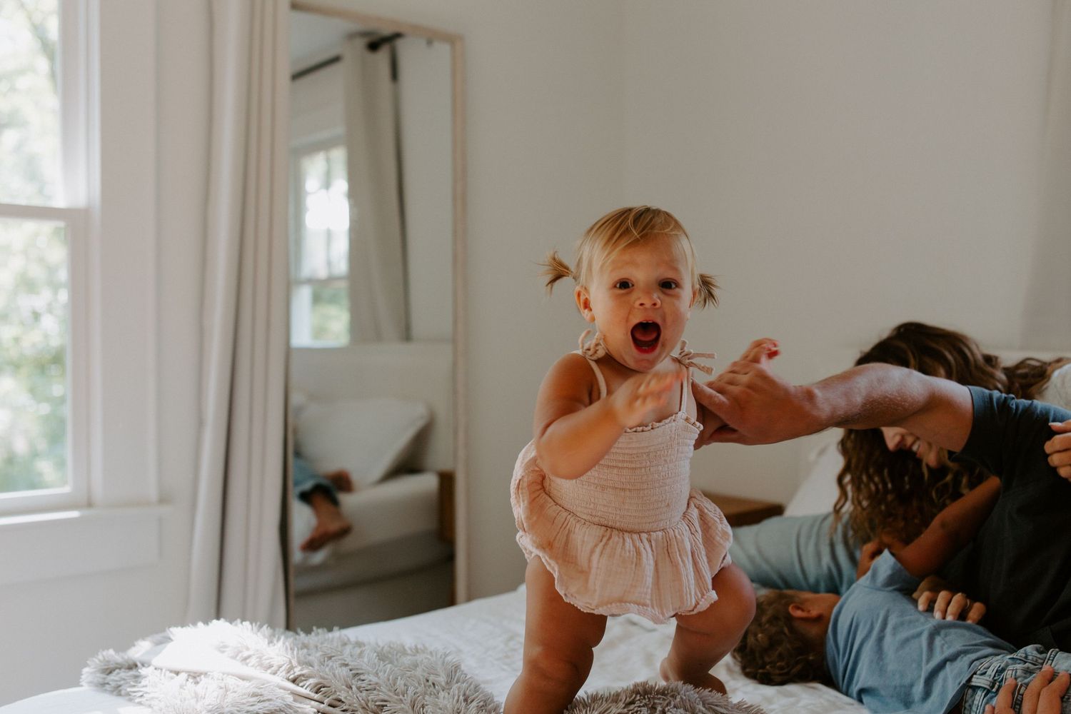 Energetic playtime moment on a bright white bed near a window.