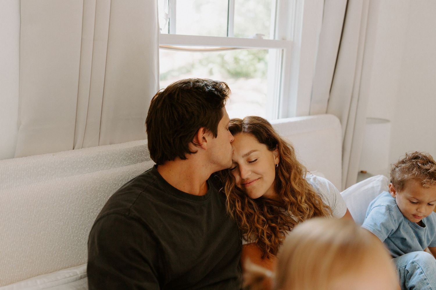 A tender kitchen dance scene with white cabinets and natural light streaming through windows.