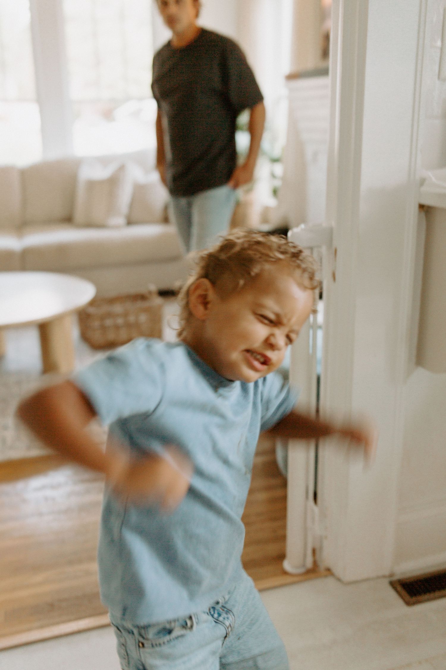 Child in light blue shirt playing energetically in sunny living room.