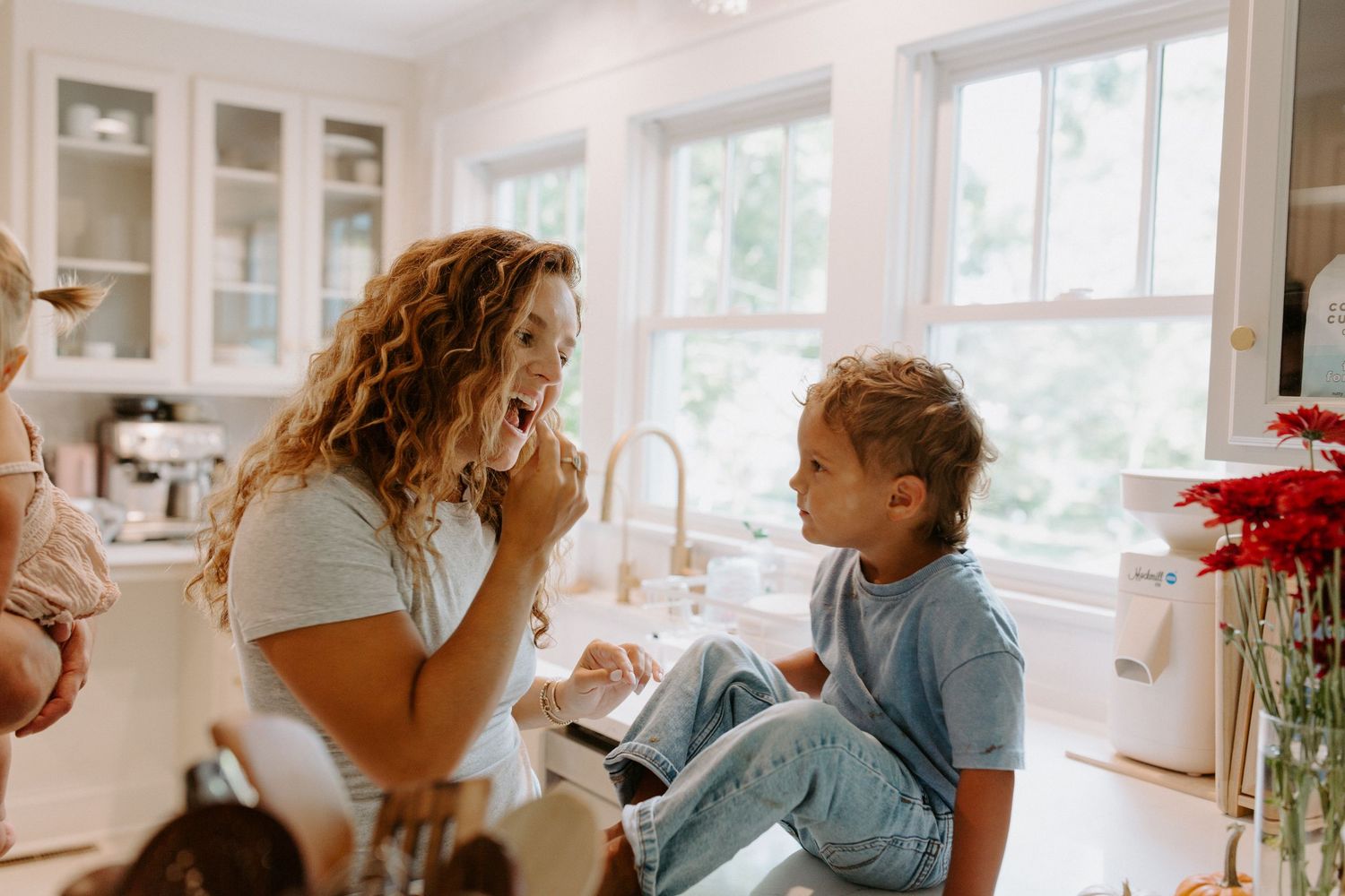 Candid moment of conversation in a sunlit kitchen with white cabinets.