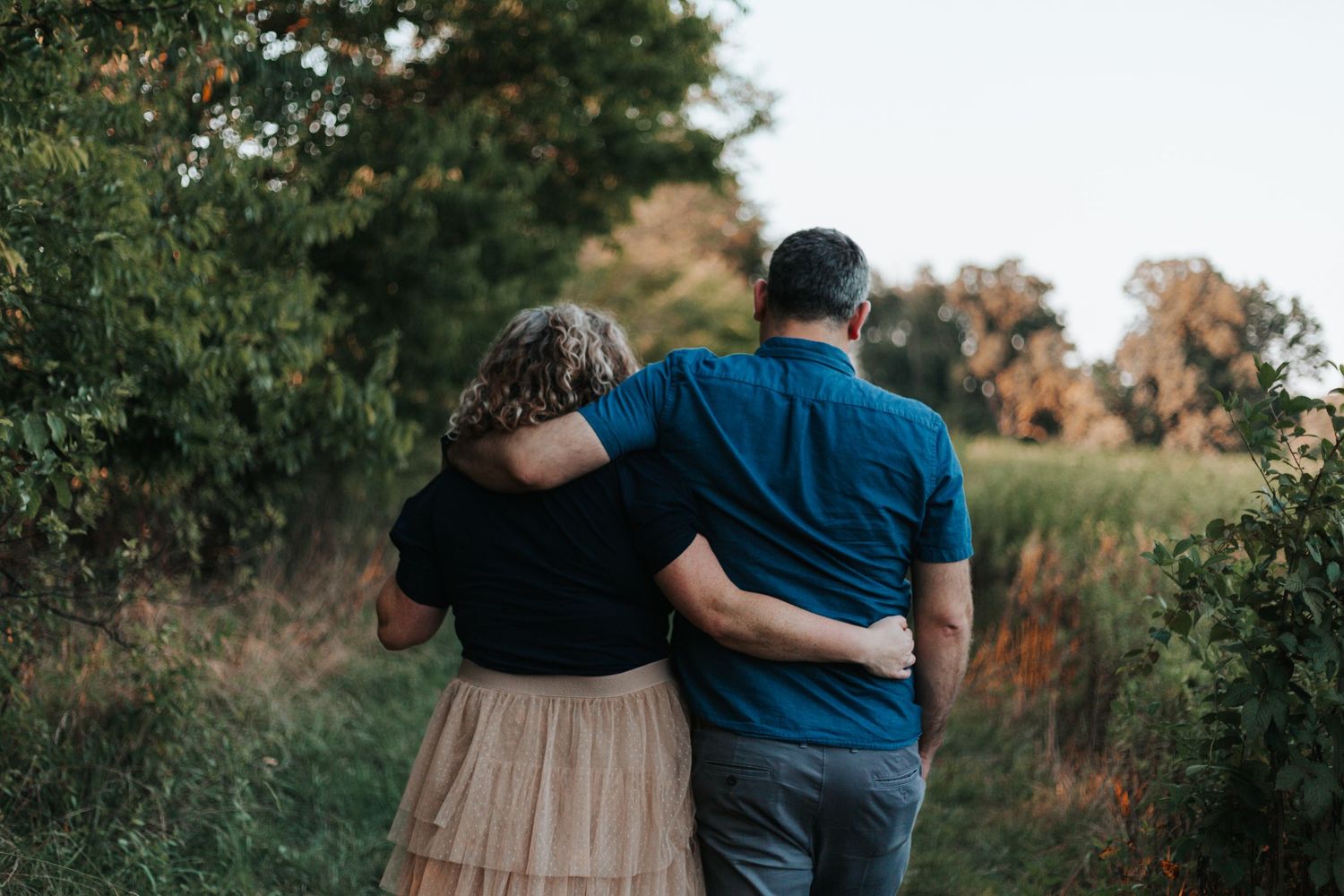 Two people embrace while walking through a park during golden hour.