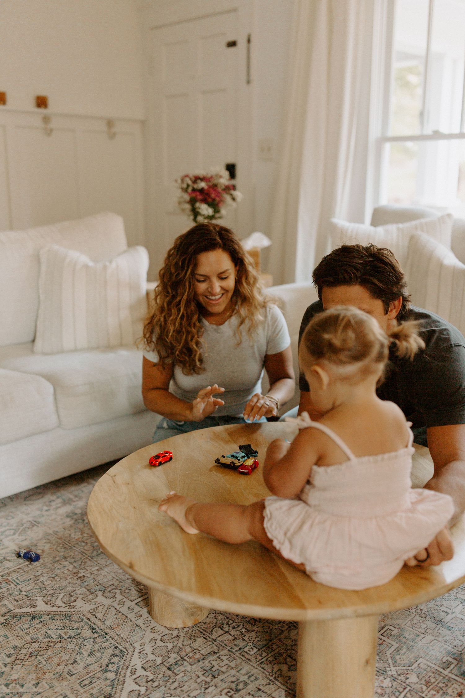 Family playing together at round wooden table in cozy white living room.