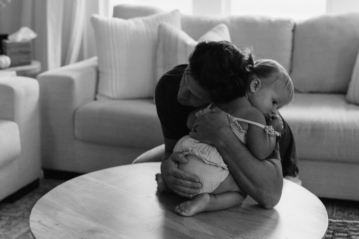 Black and white portrait of parent and child sharing an intimate moment on a sofa.