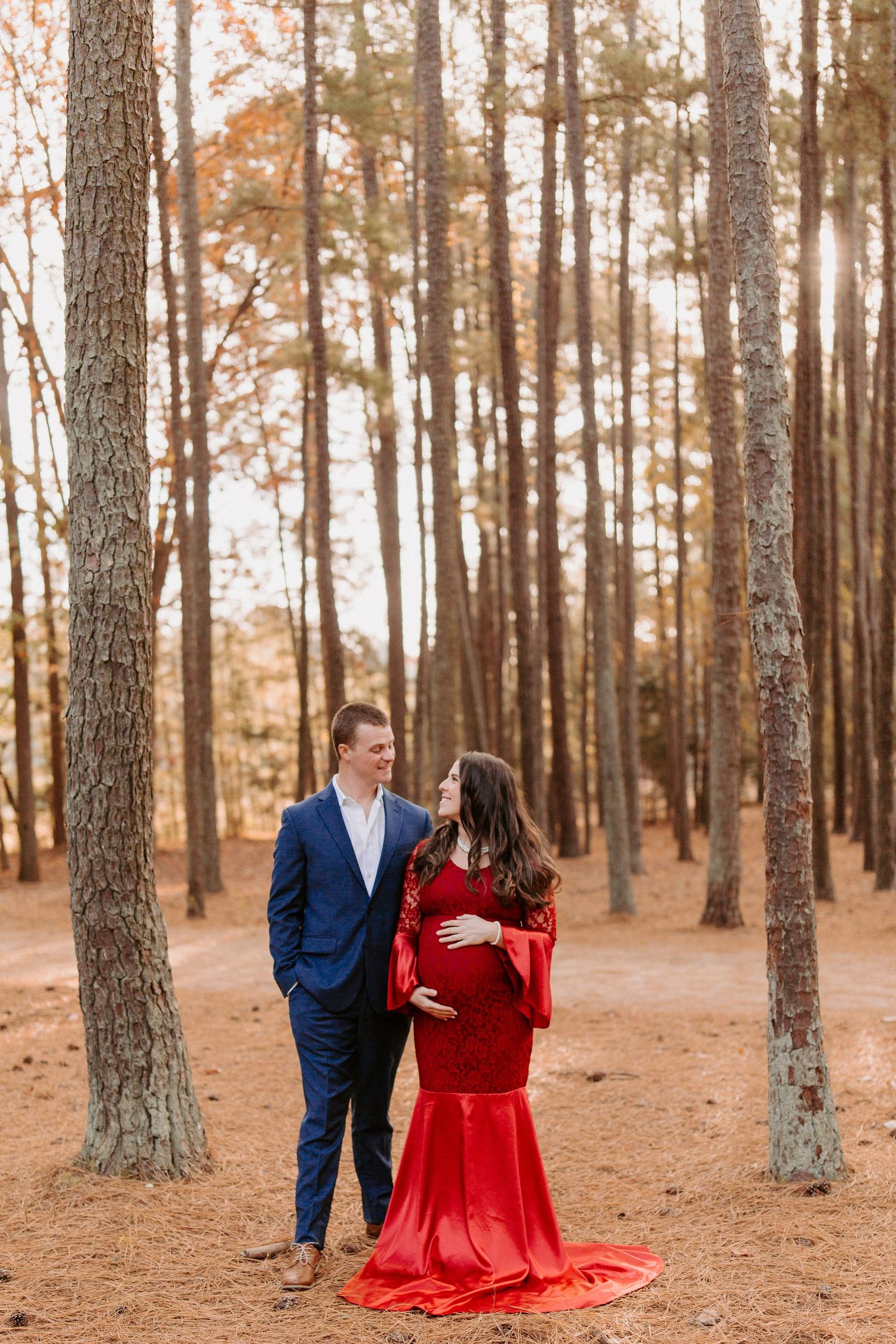 Romantic couple in pine forest with woman wearing flowing red dress.