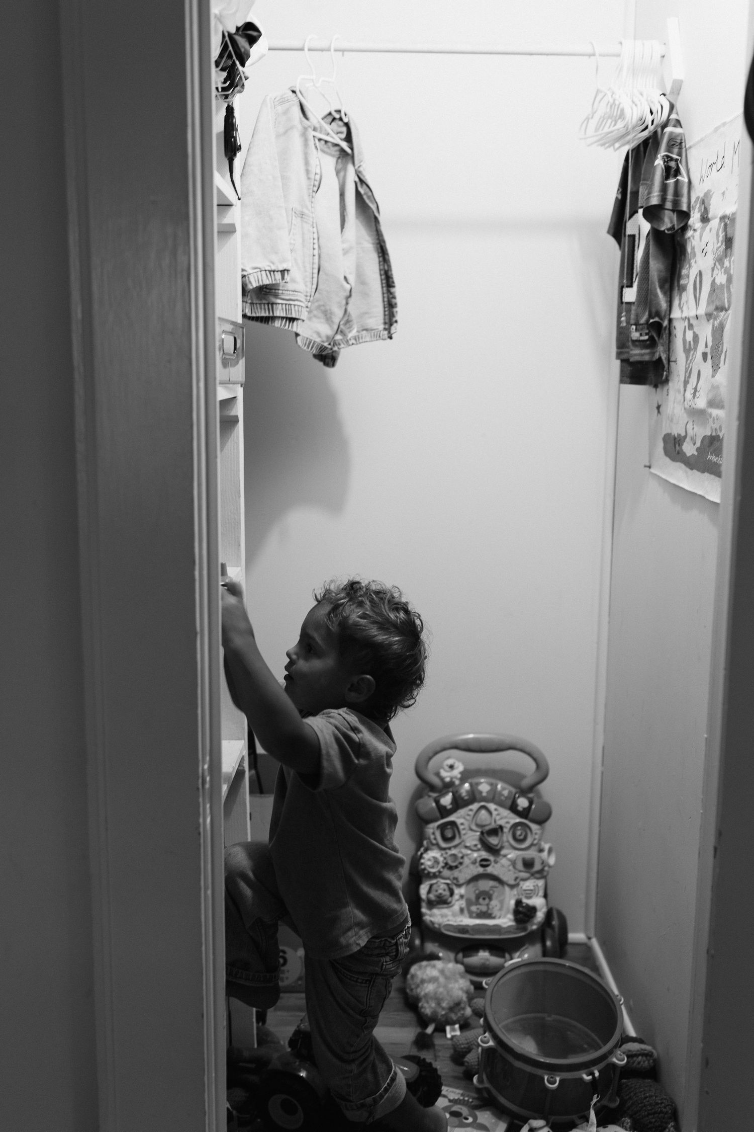 Black and white photo of reaching up to hanging items in a narrow hallway or closet space.