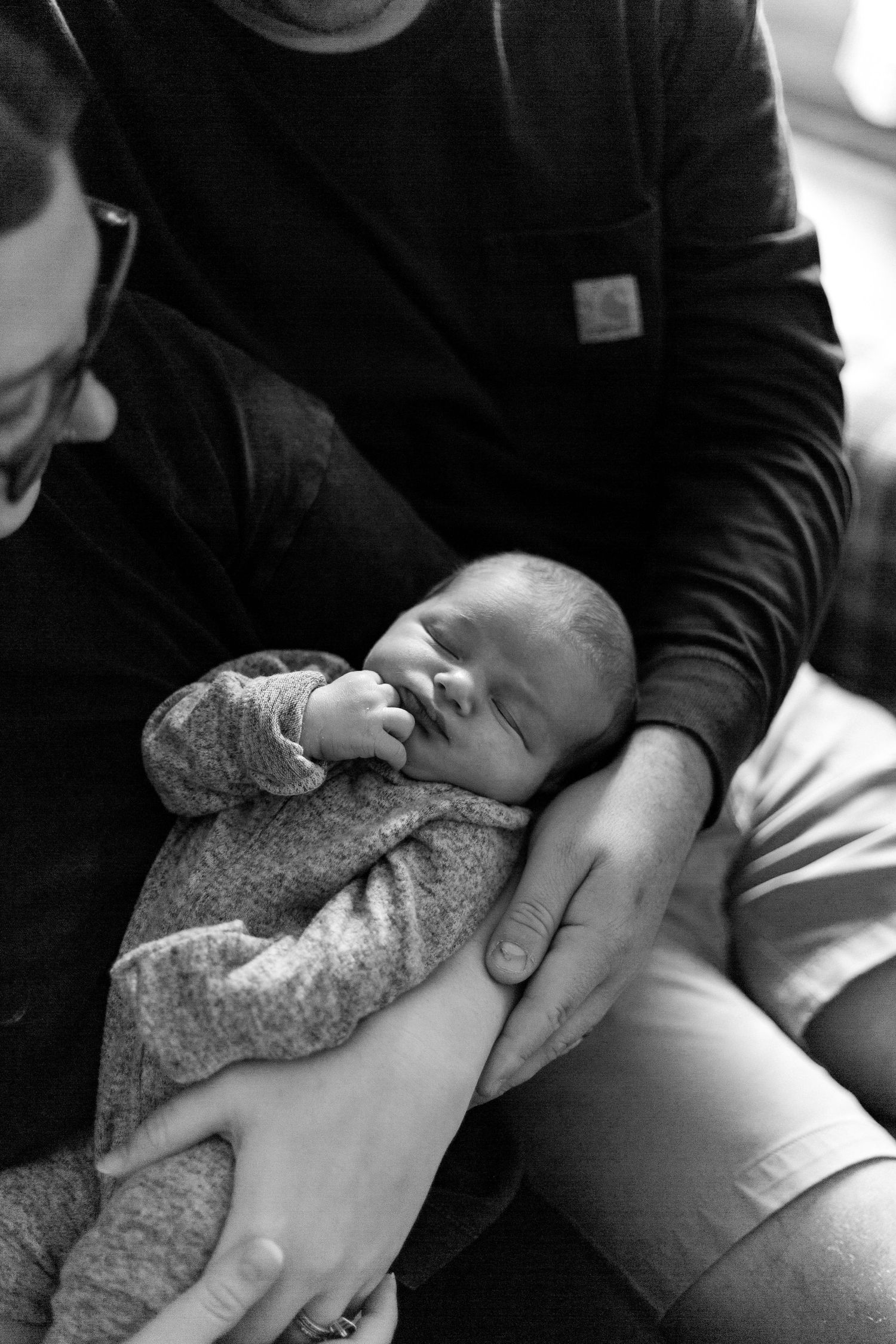 Black and white photo of sleeping newborn cradled in gentle hands.