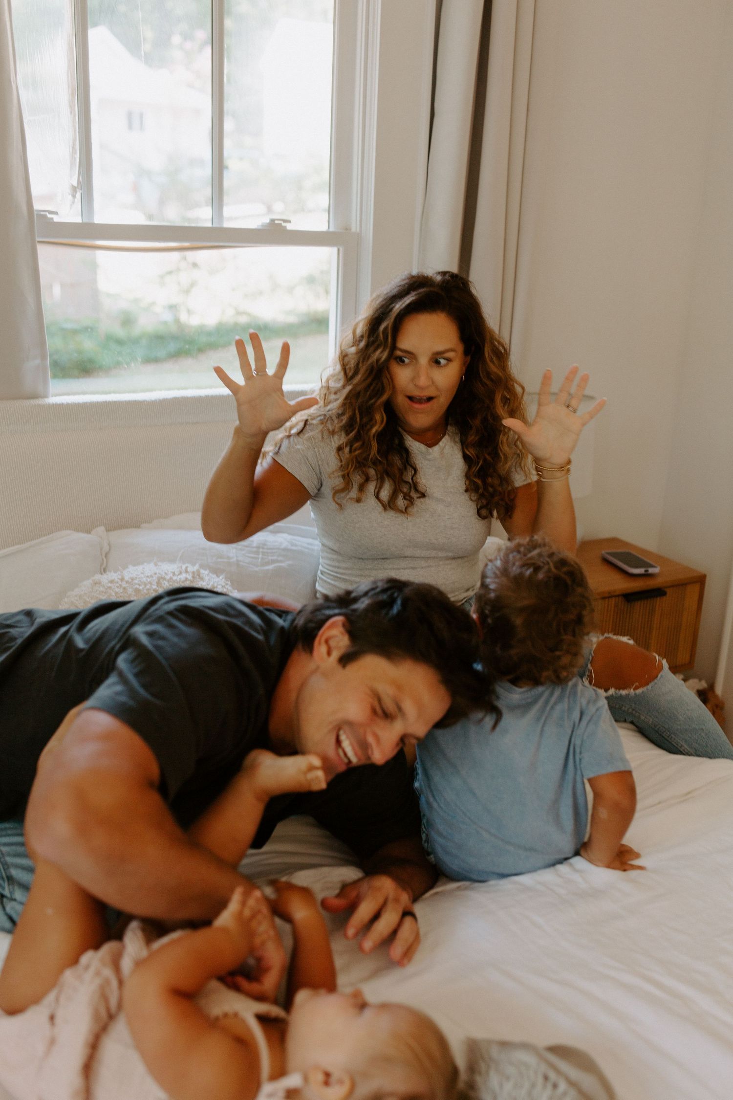 Playful family interaction with silly expressions on a white bed.