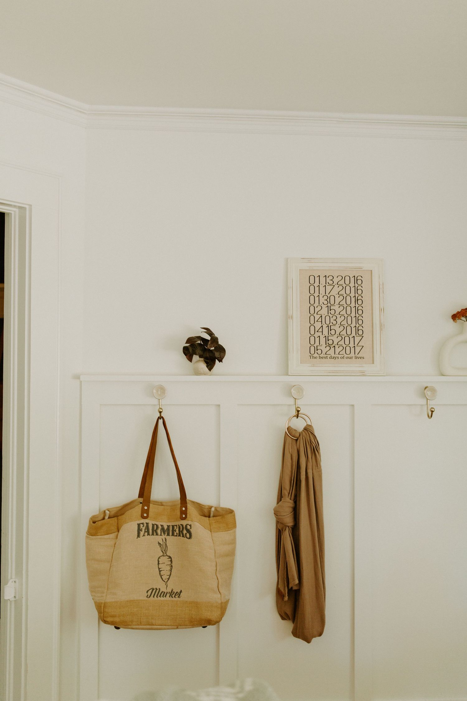 A tan farmers market tote bag and jacket hanging on white wall hooks in a bright interior space.