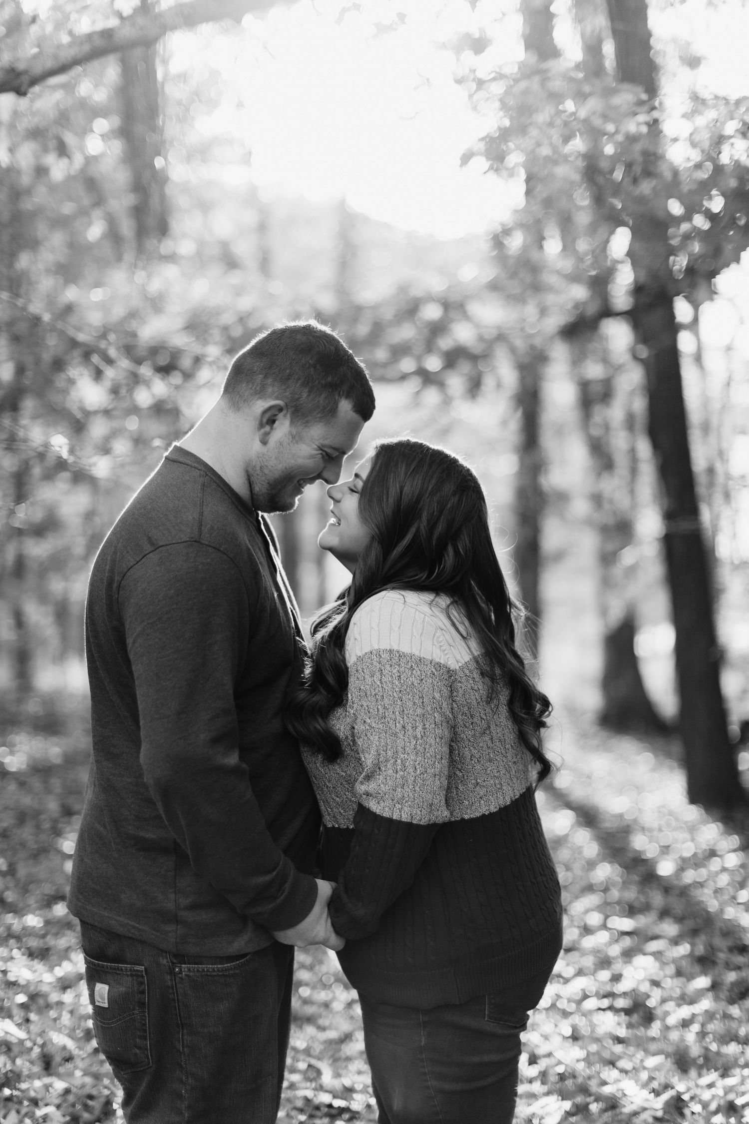 A romantic couple shares an intimate moment among autumn trees in black and white.