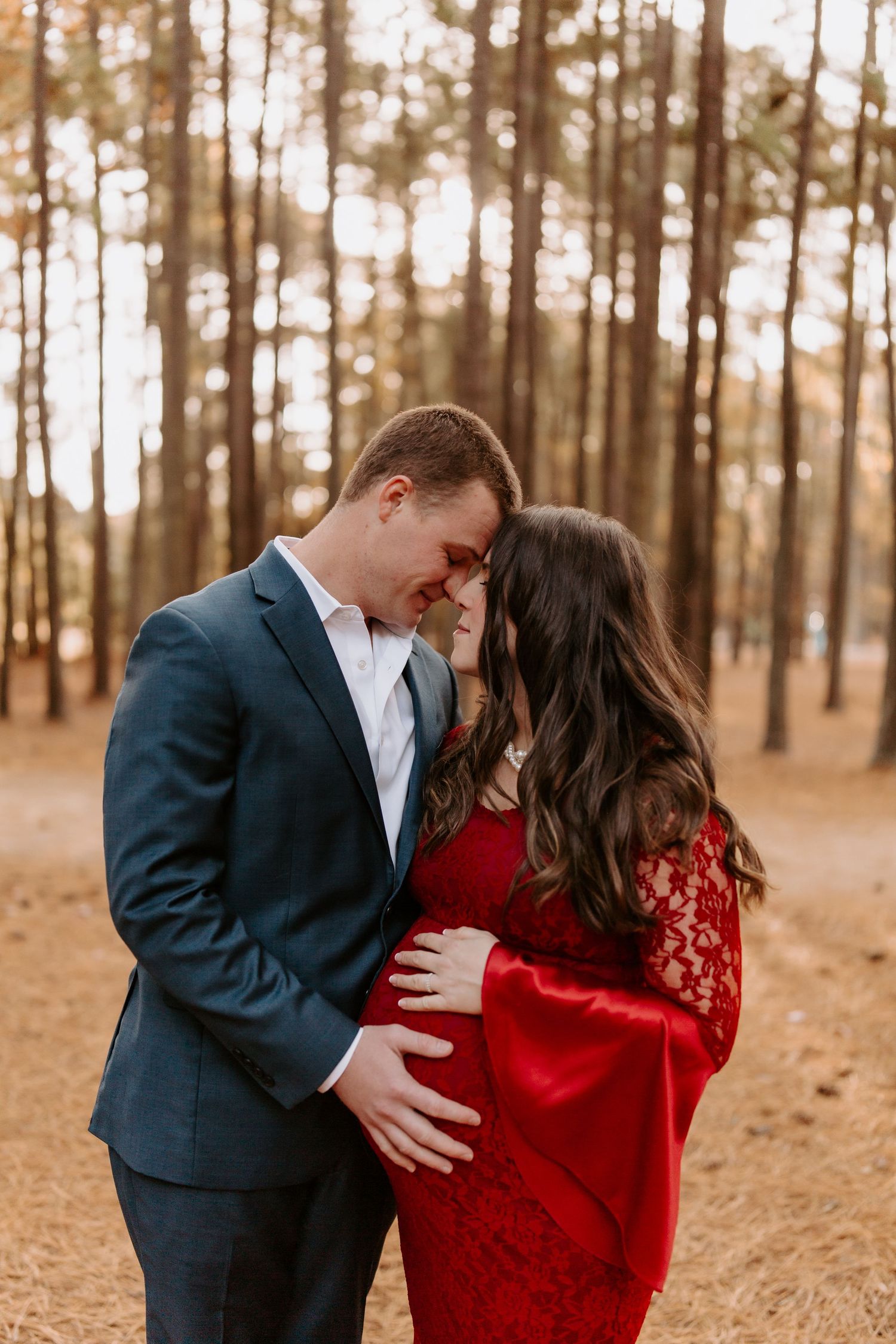 A romantic autumn photo session featuring a navy suit and red lace dress among pine trees.