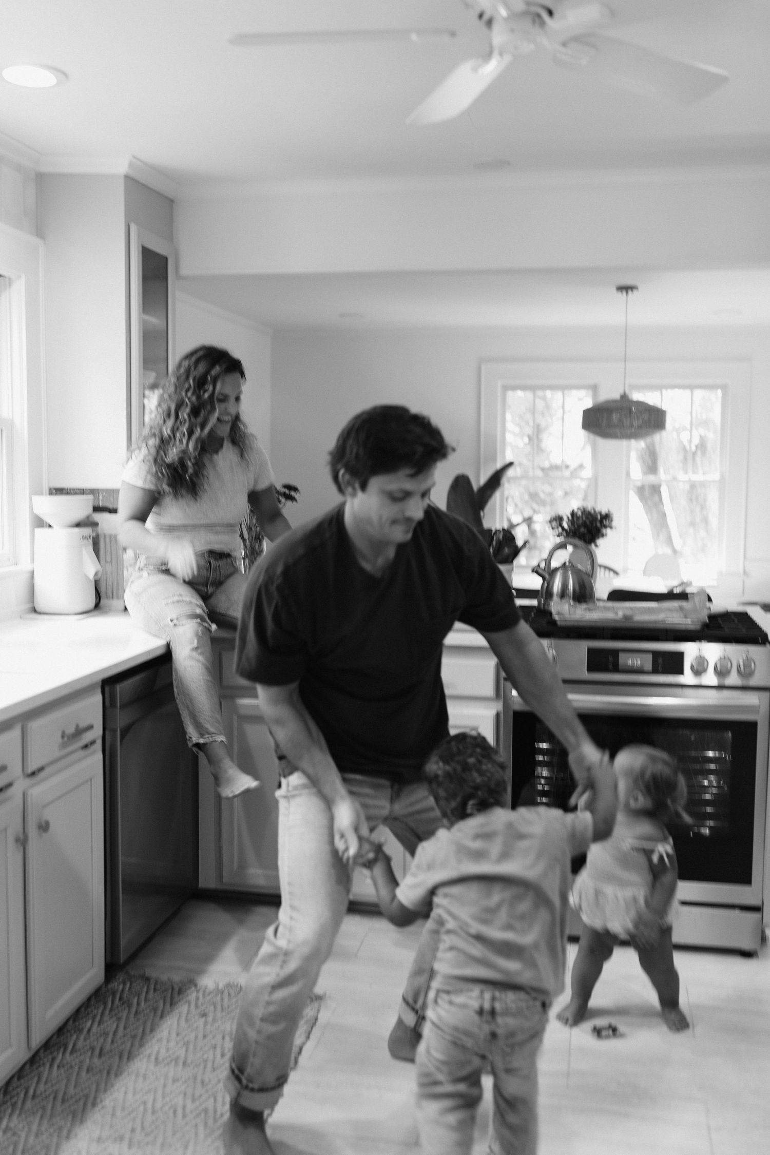 A family dances together in their bright modern kitchen with white cabinetry.