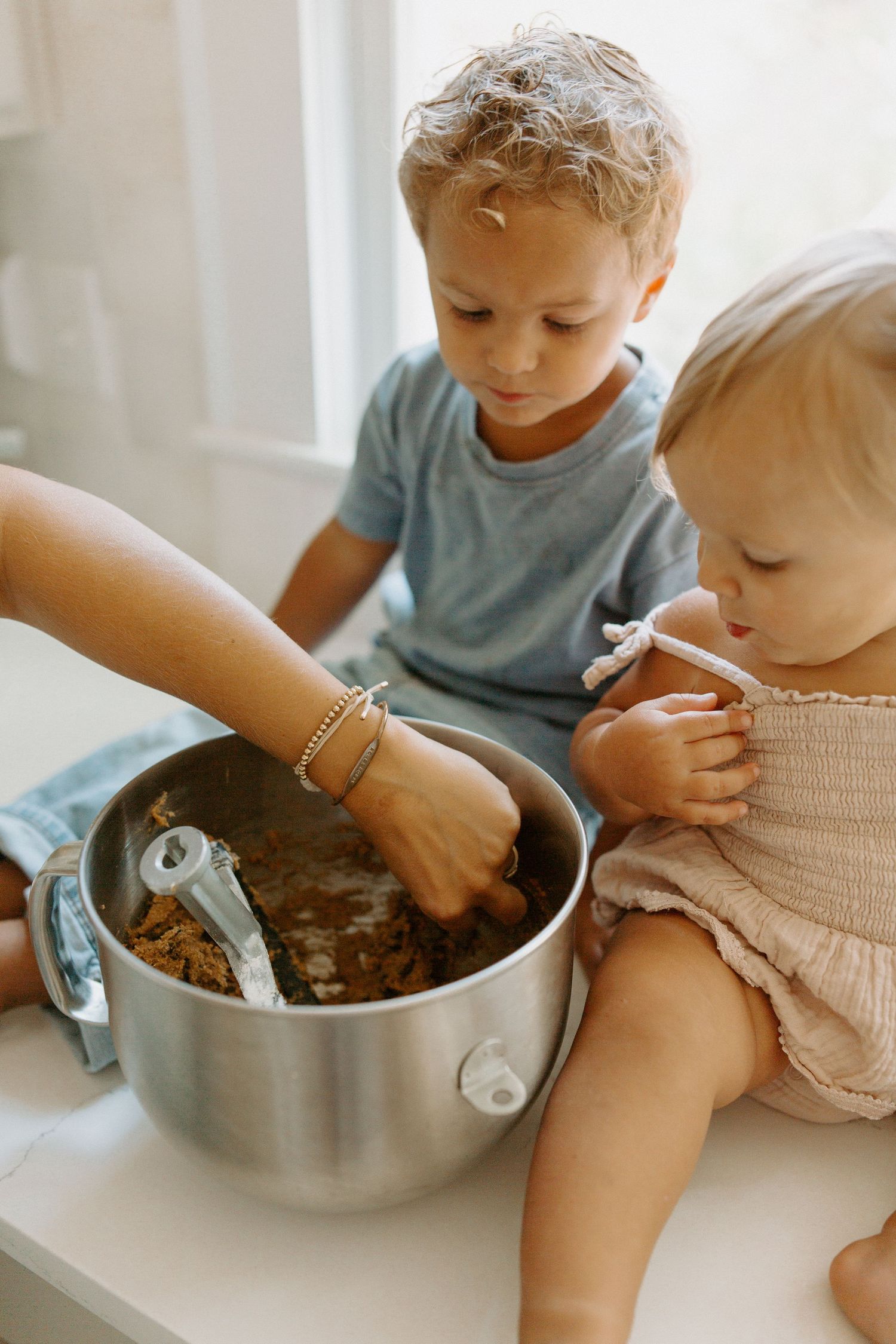 Two children watching intently as someone mixes ingredients in a large metal bowl.