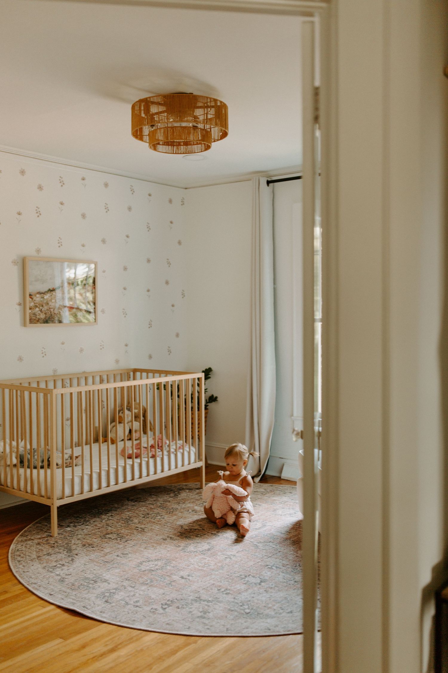 A minimalist nursery with round rug, wooden crib, and polka dot wallpaper.
