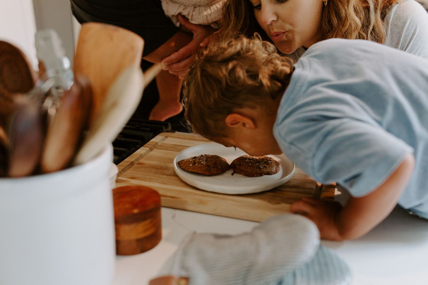 Hands reaching for freshly baked cookies on a wooden cutting board.
